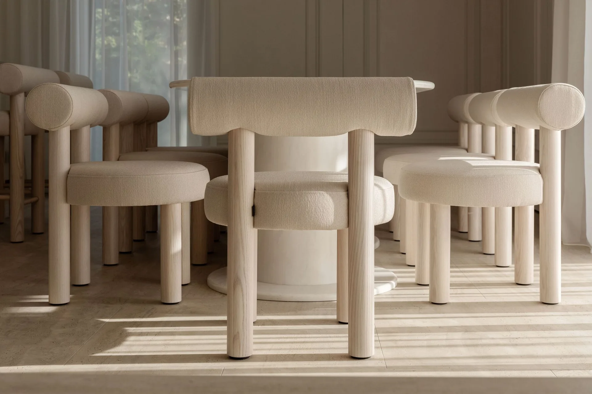 Modern dining chairs with chunky cylindrical wood legs and cream upholstered seats are arranged around a pedestal table on a beige tiled floor.