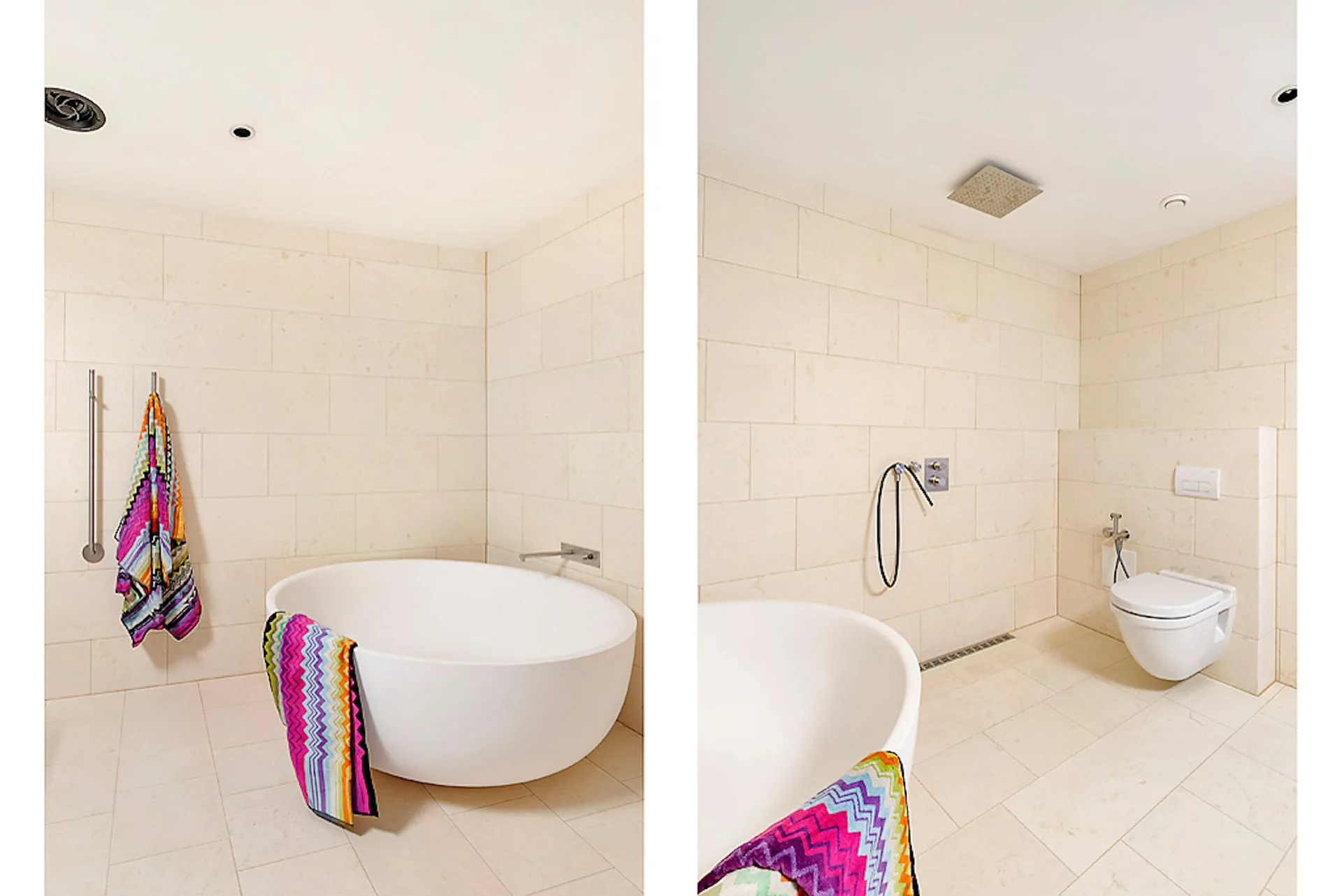 A modern bathroom clad in large beige stone-look tiles featuring a round white freestanding bathtub and a wall-mounted toilet.
