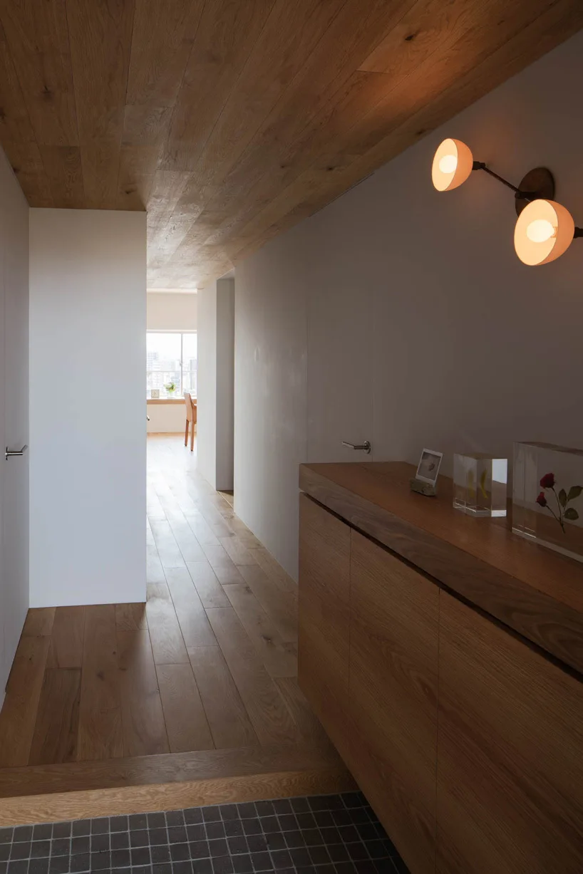 A minimalist hallway features matching wood plank floors and ceilings, a wooden console cabinet, and a glowing warm wall sconce.