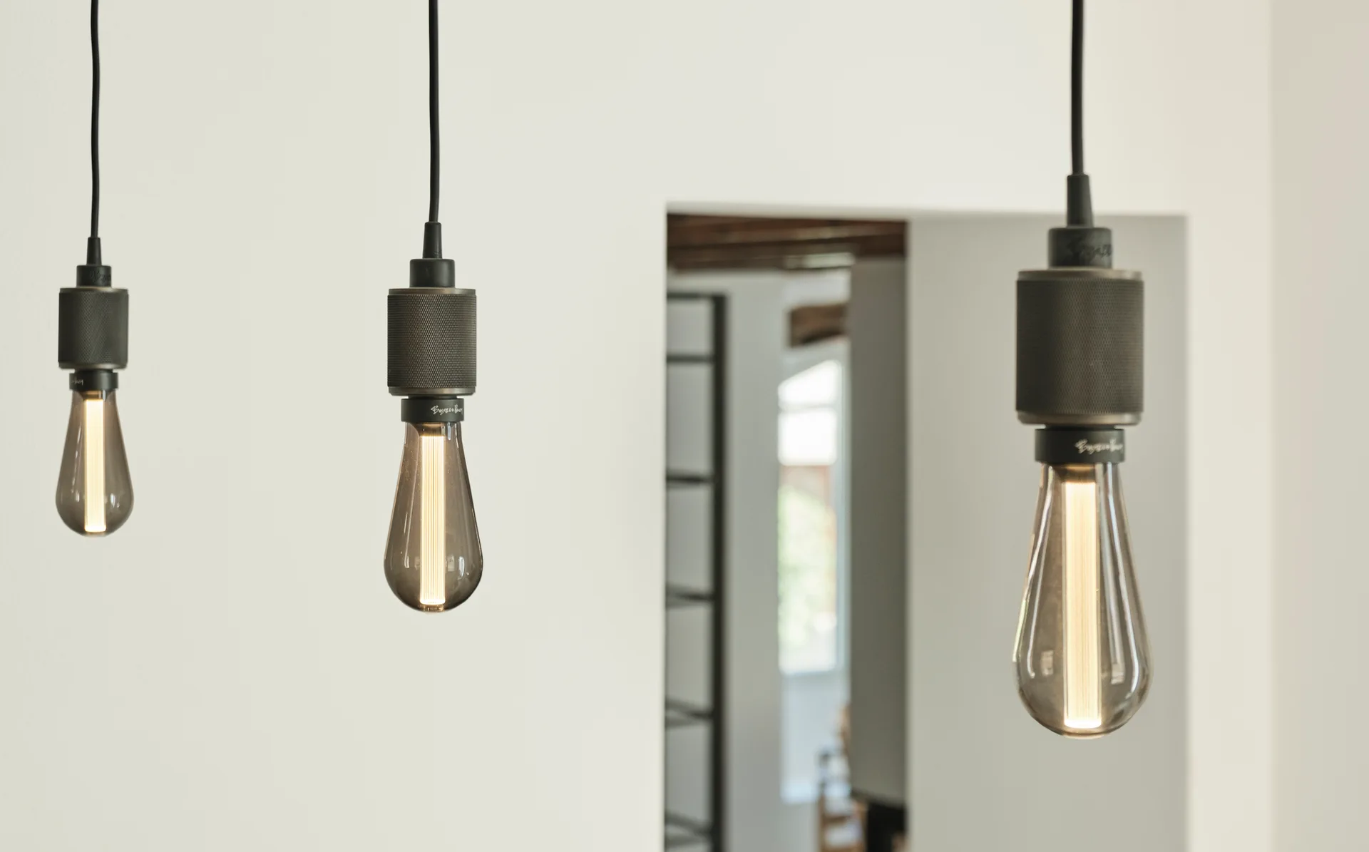 Three industrial pendant lights with black textured sockets and glowing filament bulbs hang at staggered heights against a white wall.