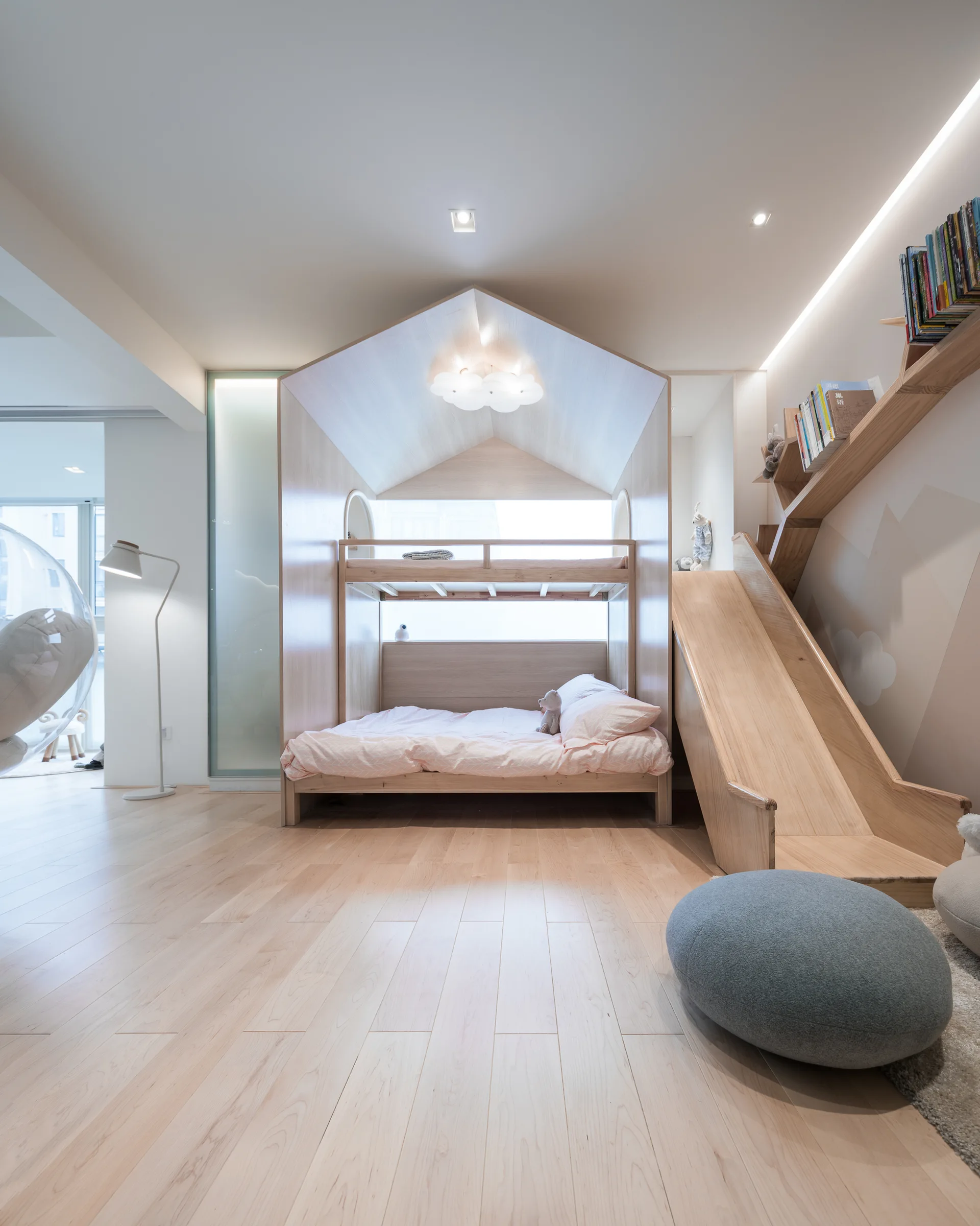 A light wood house-shaped bunk bed with an integrated slide dominates a children's bedroom featuring a mountain mural and light wood flooring.