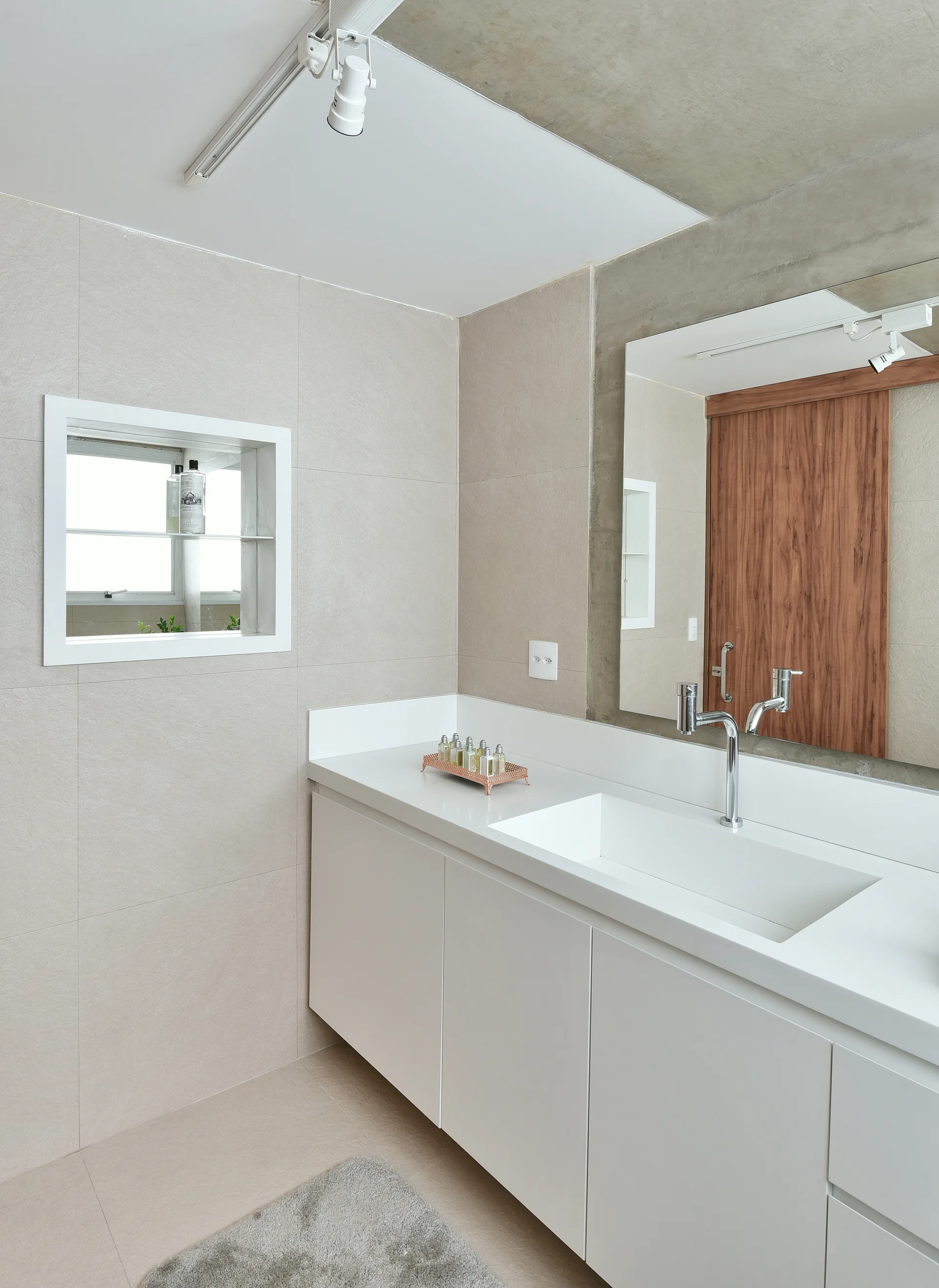 A minimalist bathroom with a white floating vanity, integrated sink, and large wall mirror against beige tile walls.