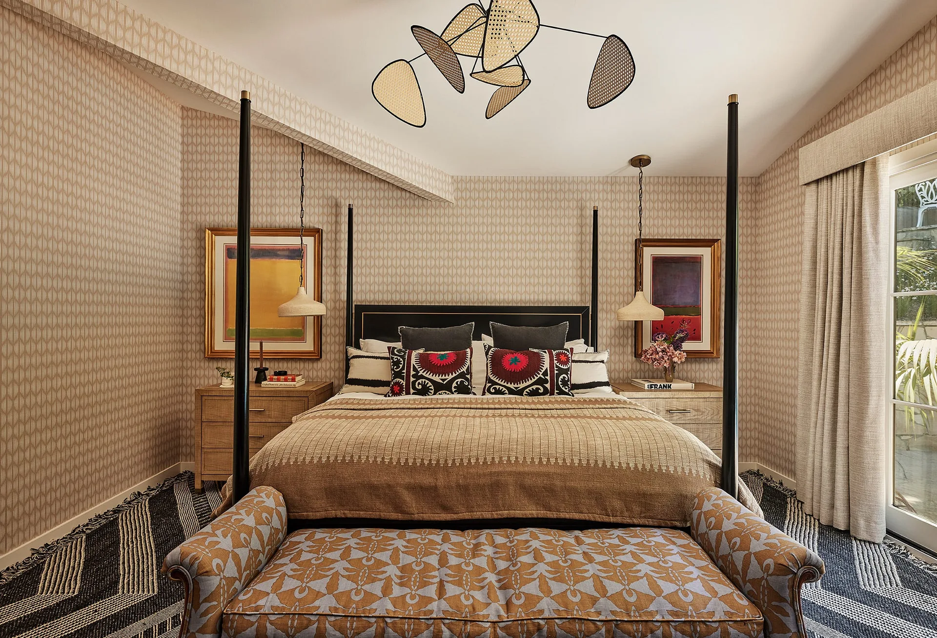 A bedroom featuring a black four-poster bed, geometric wallpaper, matching wood nightstands with hanging pendants, and a sculptural ceiling light fixture.