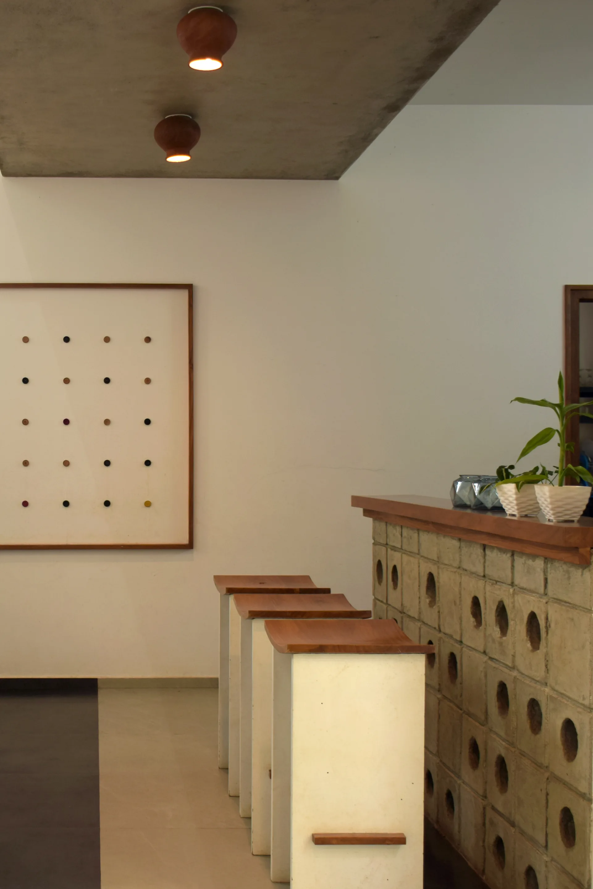 Three minimalist wood-topped stools line a concrete breeze block bar counter under warm ceiling lights in a modern interior.