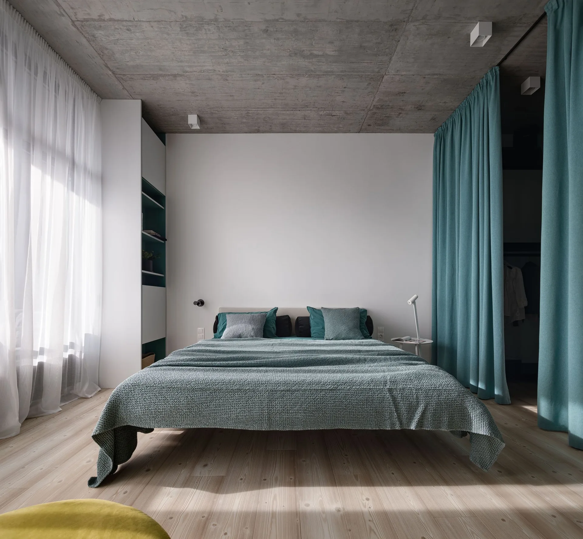 A minimalist bedroom features a bed with teal bedding under an exposed concrete ceiling, complete with sheer window curtains and a teal room divider curtain.