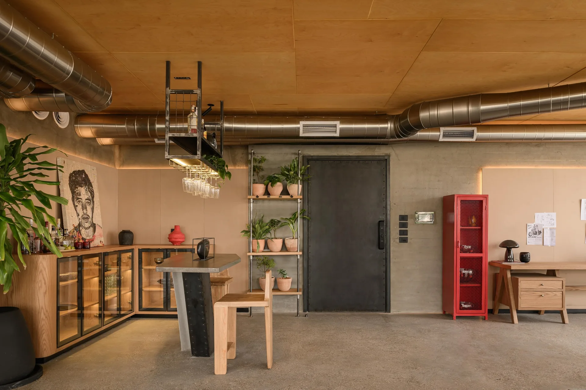An industrial interior features concrete walls, exposed metal ductwork, a wood-paneled ceiling, glass-front cabinets, and a red metal mesh locker.