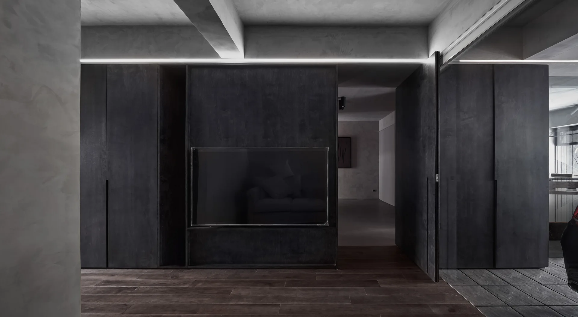 A minimalist living space featuring dark charcoal wood cabinetry with an integrated television under a concrete ceiling.
