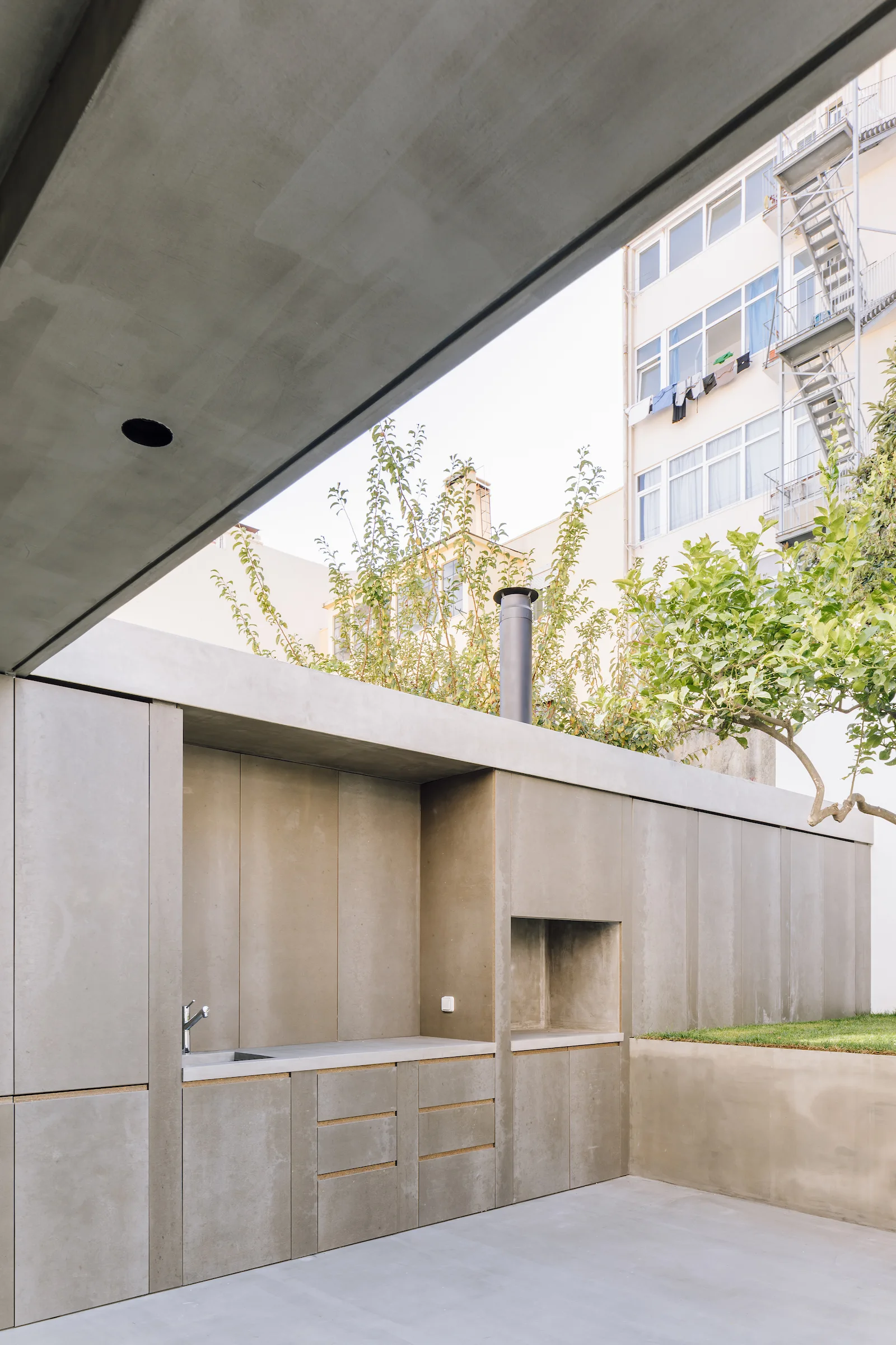 A minimalist outdoor concrete kitchen with an integrated sink and built-in grill area on a stone patio.