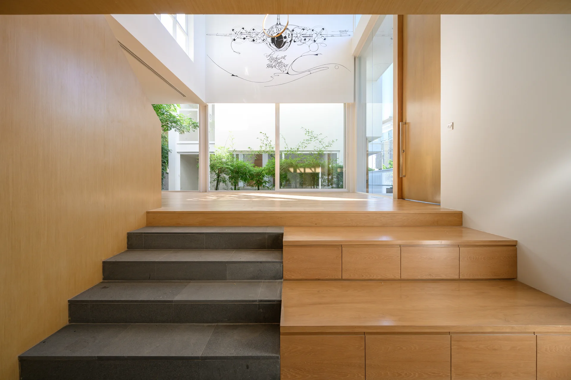 A minimalist entryway staircase combines dark stone steps with light wood stairs featuring integrated drawer storage below a large window.