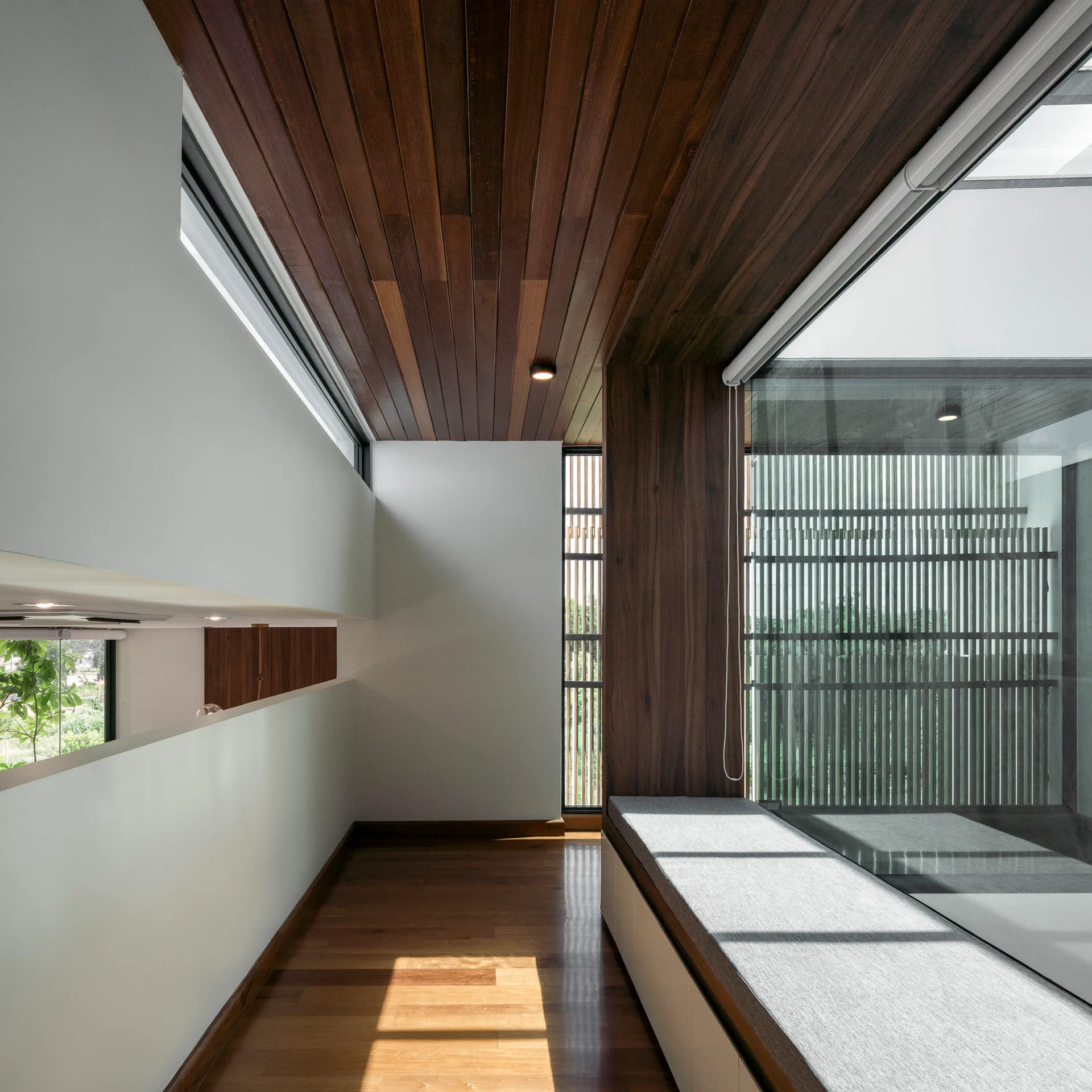 A minimalist hallway landing features a rich wood plank ceiling and floor with a built-in window bench next to large windows.
