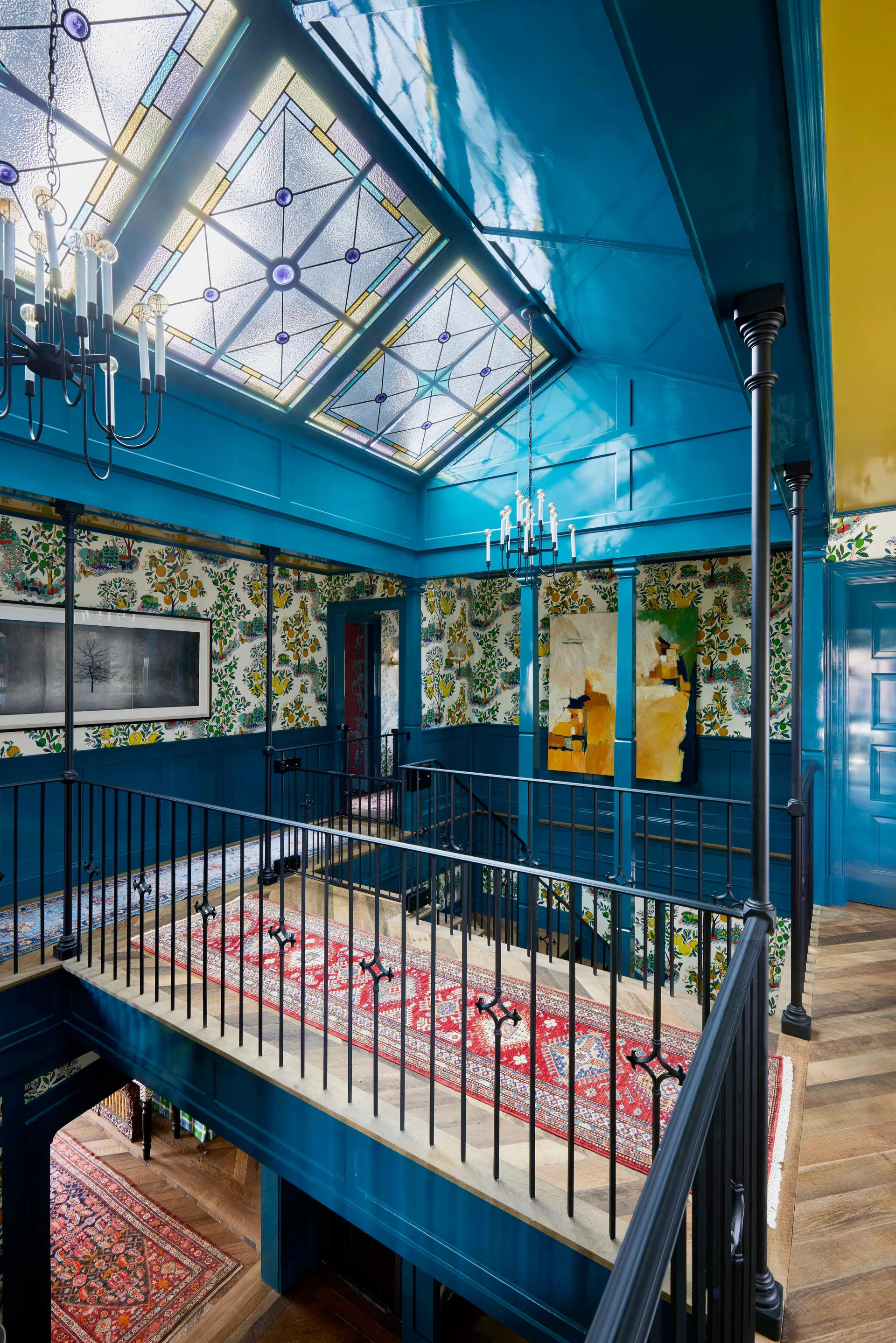 A residential staircase landing features high-gloss teal trim, decorative floral wallpaper, a red runner rug, and a stained glass skylight.