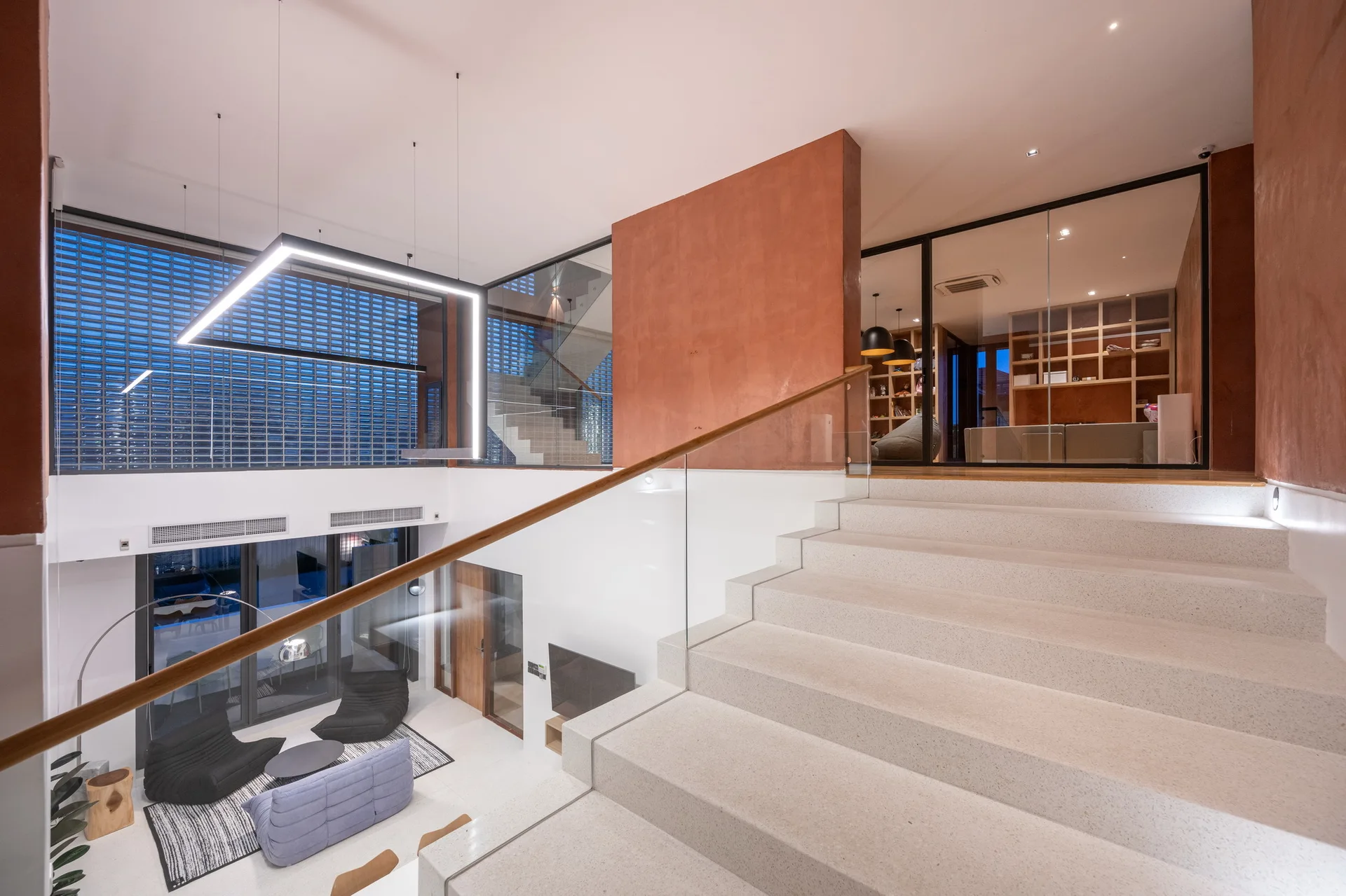 A wide stone staircase with a glass railing leads to an upper landing featuring a terracotta plaster wall and glass partitions.