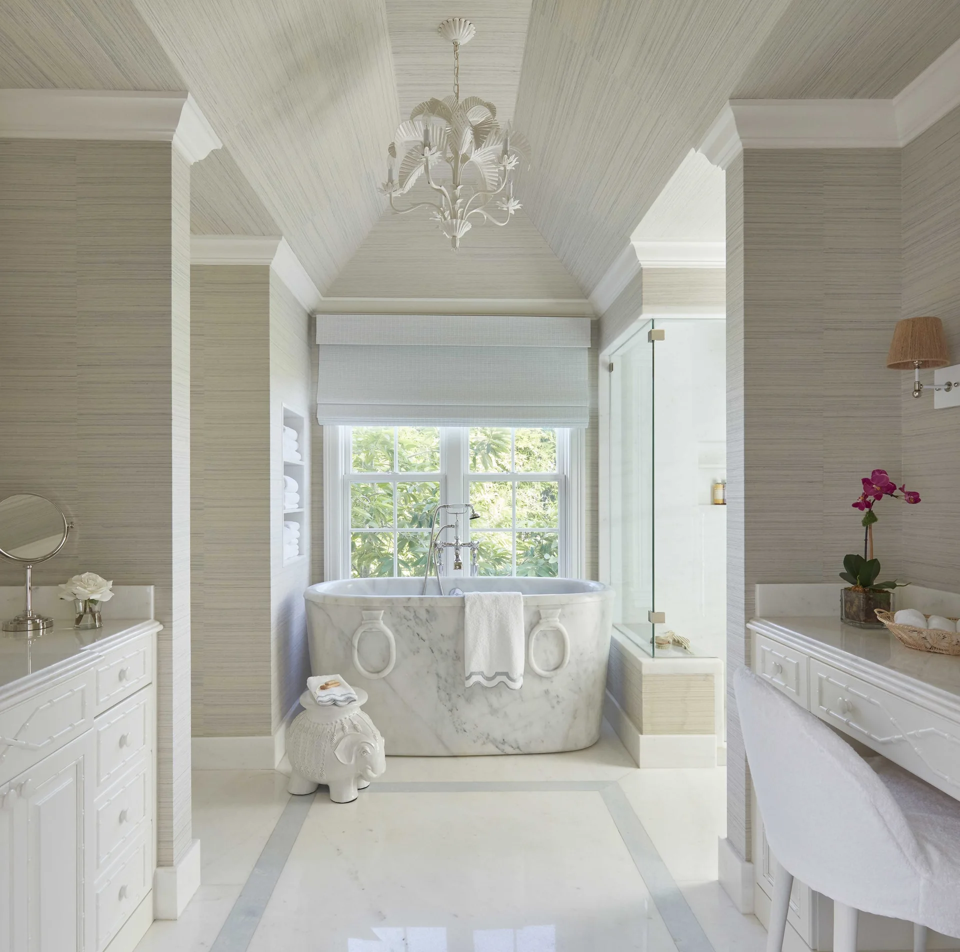 A symmetrical bathroom featuring a central marble freestanding bathtub beneath a vaulted ceiling covered in textured grey wallpaper.