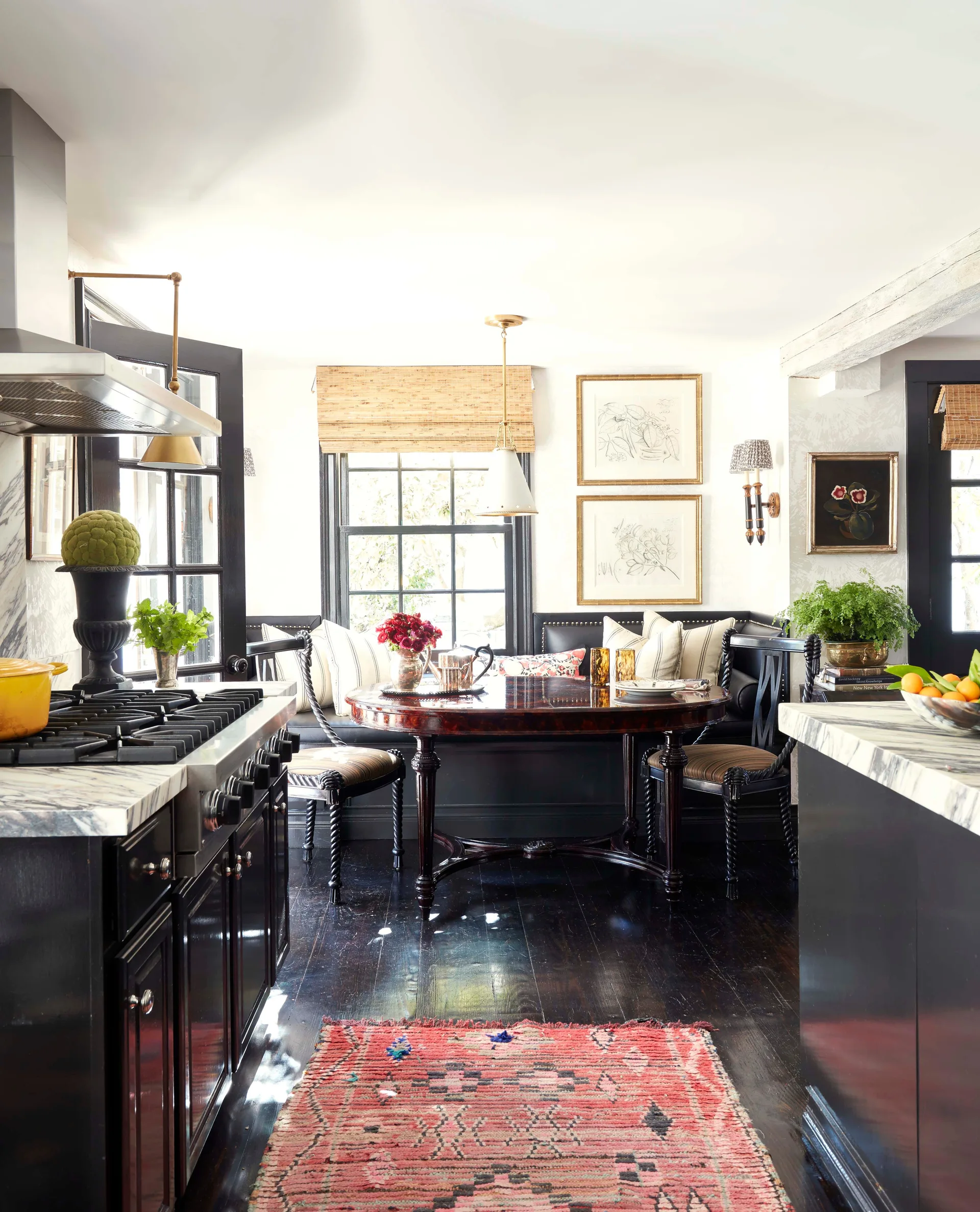A kitchen featuring a black leather banquette dining nook, a round wood table, marble-topped counters, and dark wood floors with a red patterned rug.