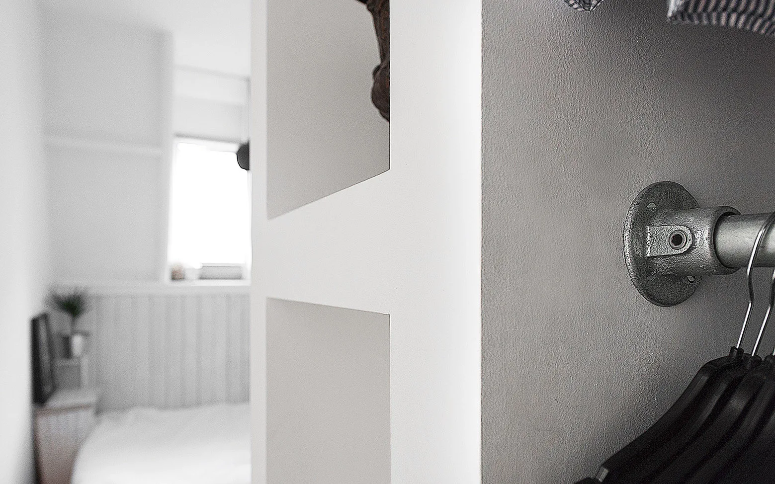 A close-up of a galvanized metal pipe clothing rod mounted to a grey wall with black hangers in a minimalist closet.