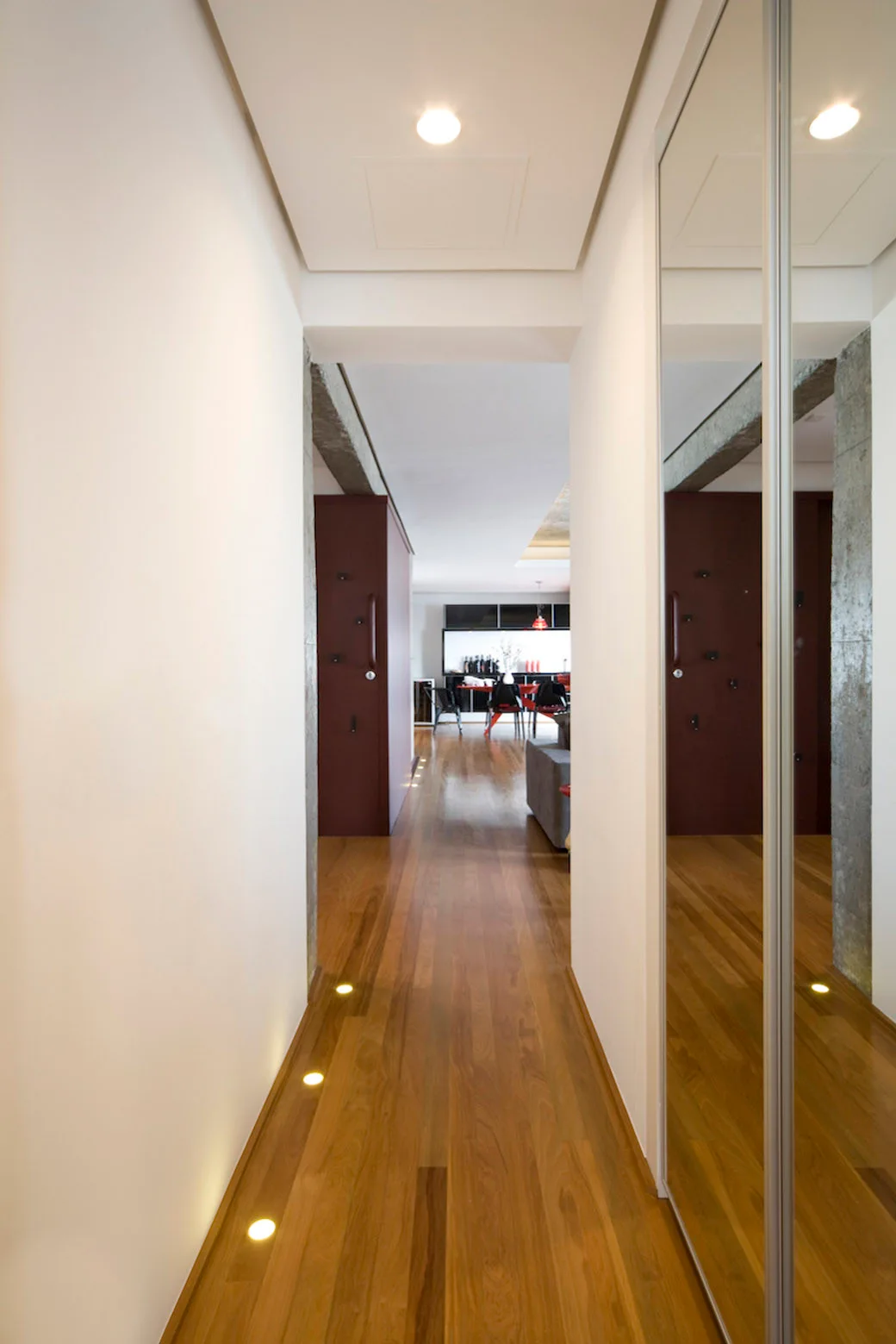A long interior hallway features warm wooden flooring, recessed spotlights along the lower left wall, and a large mirrored panel on the right.