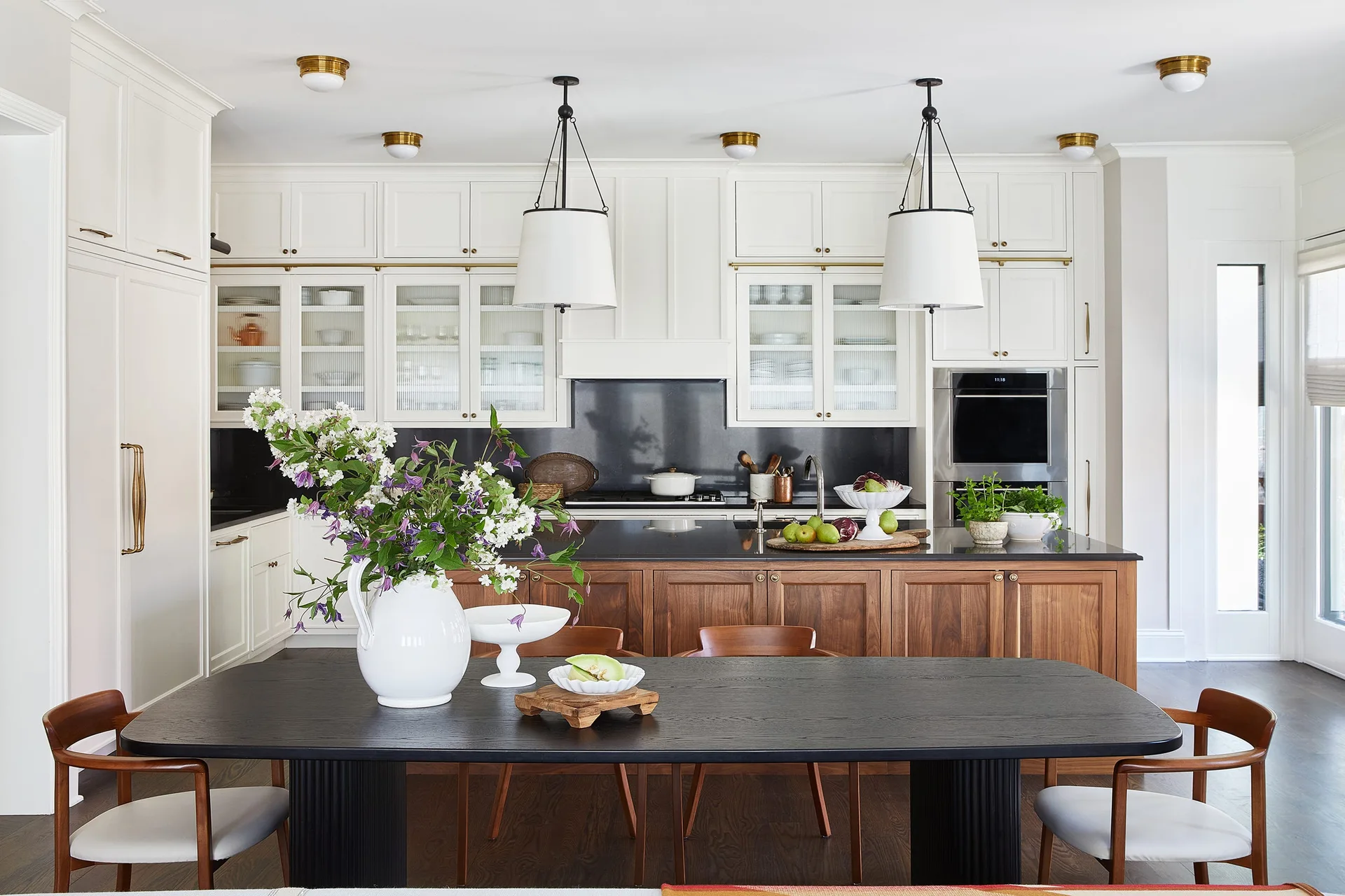 A kitchen featuring a walnut island with black countertops, white upper cabinets, and a black dining table in the foreground.