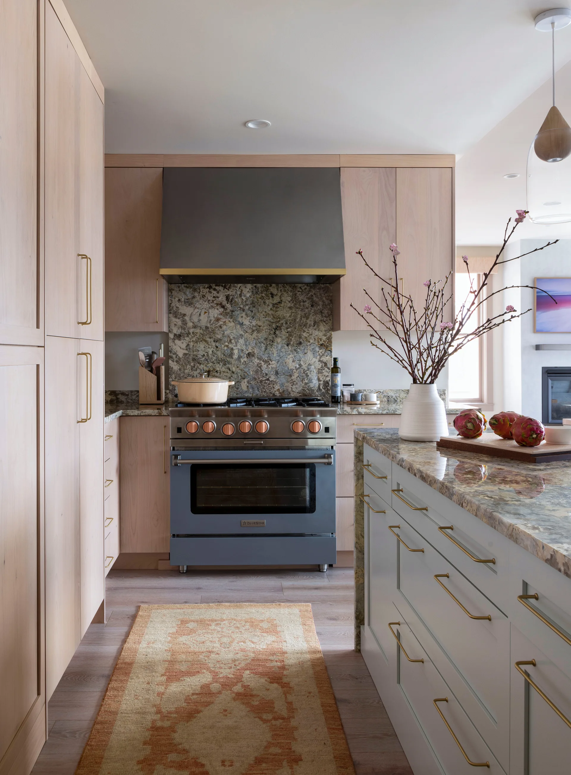 A modern kitchen with light wood cabinetry, a slate-blue range stove, matching granite countertops, and a stone-topped island.