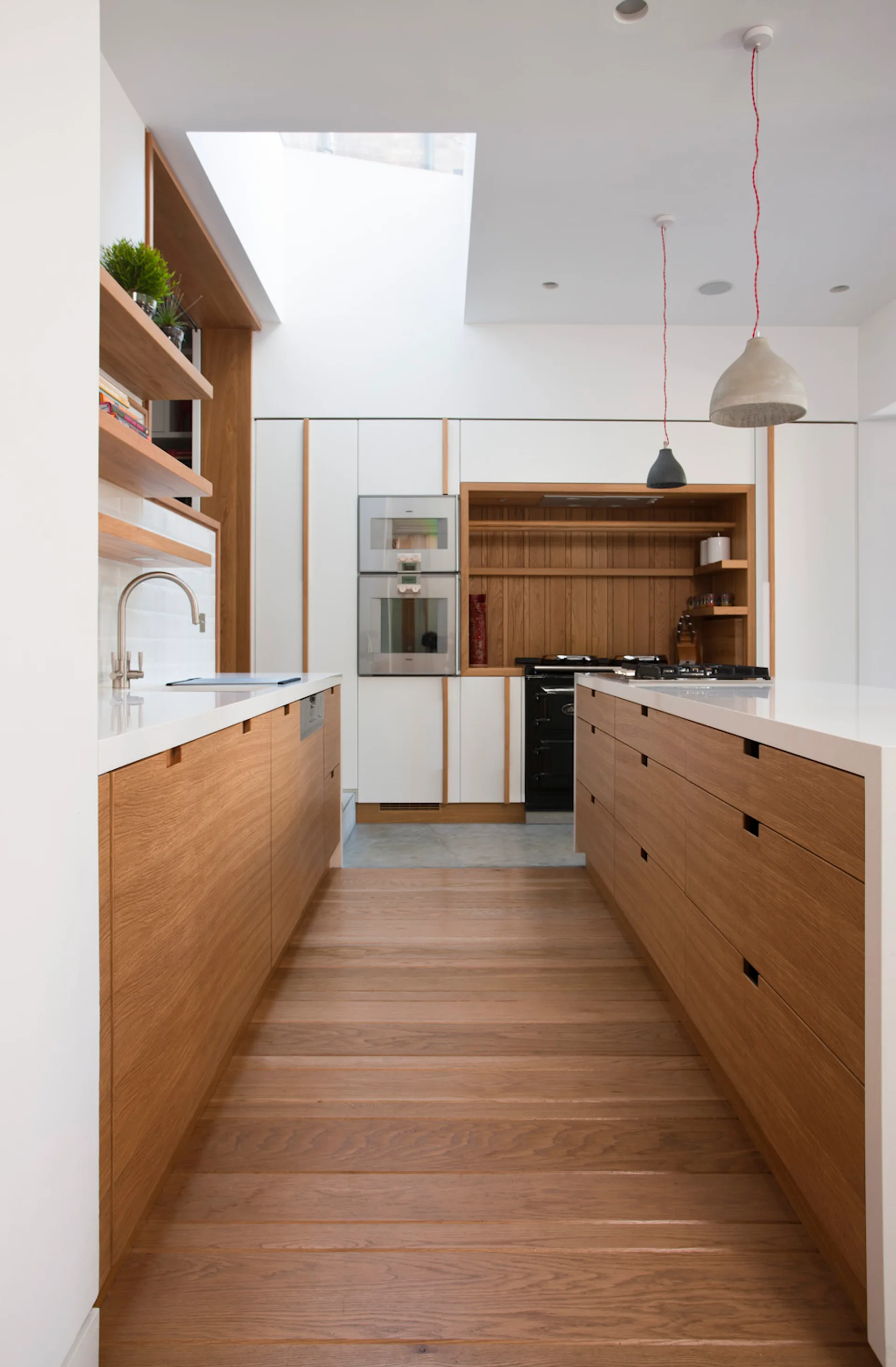 A modern kitchen featuring wood grain cabinets, a central island with a white countertop, wooden floors, and a bright overhead skylight.