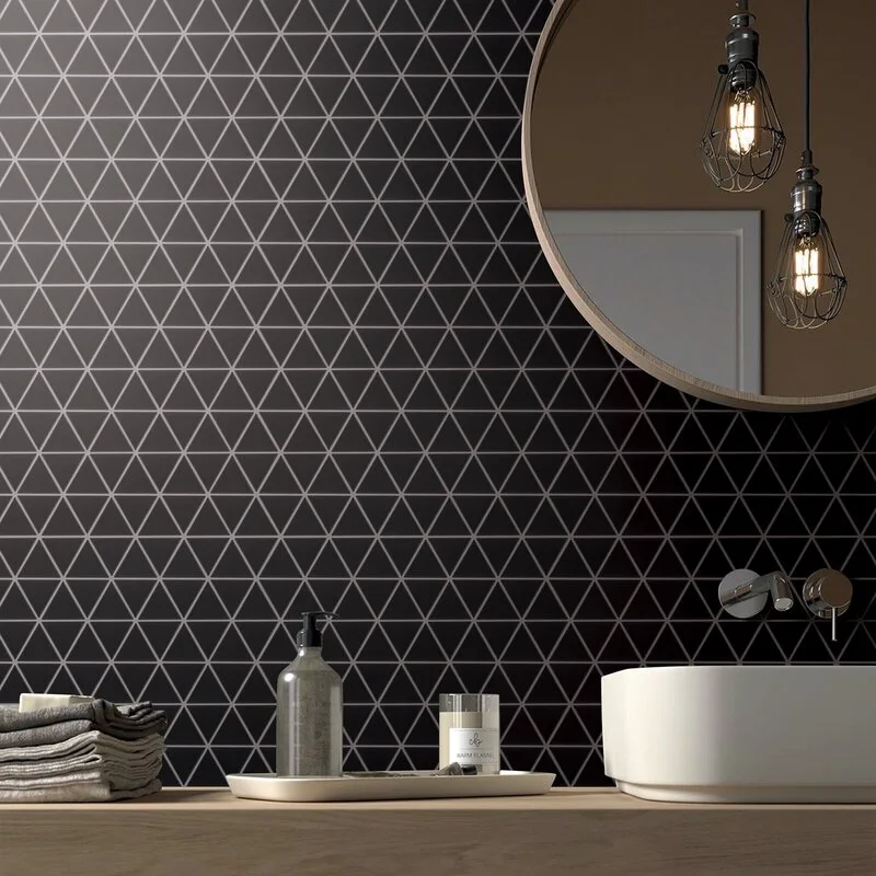 A modern bathroom vanity featuring a white vessel sink on a wood countertop against a black geometric triangle tiled wall with a circular mirror.