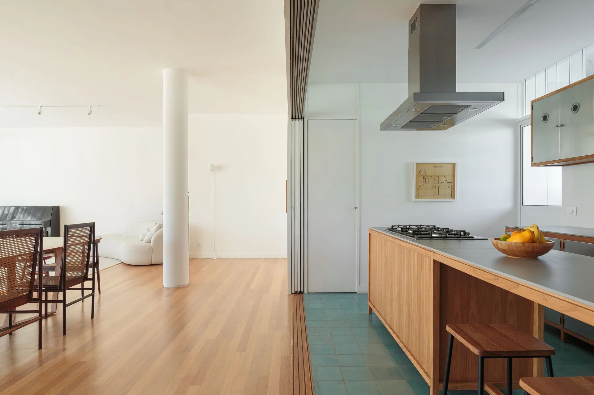 An open-concept kitchen featuring a wooden island with teal floor tiles transitions into a spacious living room with warm hardwood flooring.