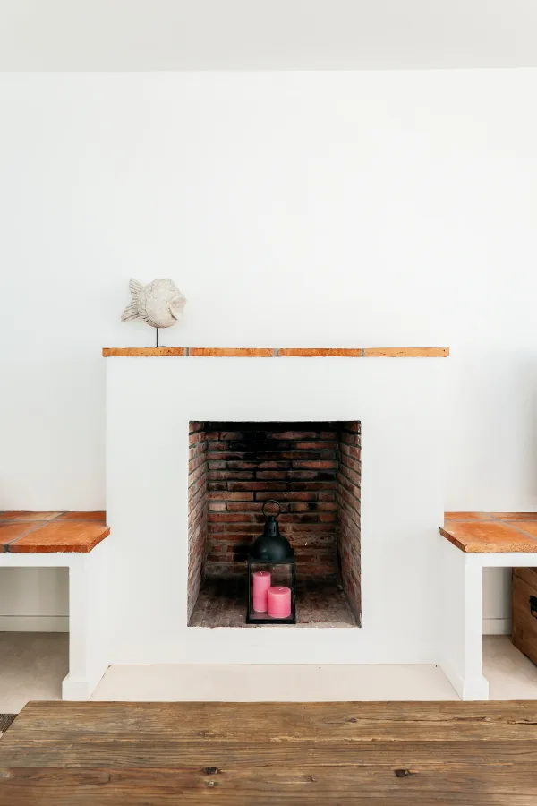 A white masonry fireplace with a red brick interior flanked by built-in benches topped with terracotta tile.