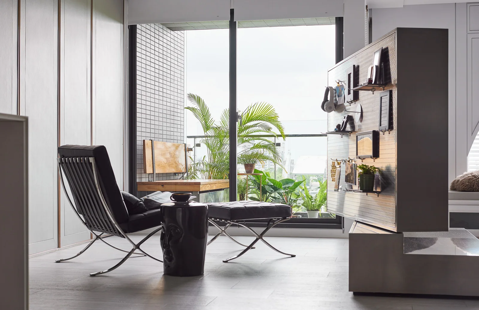 A black leather lounge chair and ottoman sit next to a tall metal pegboard room divider in front of a sliding glass balcony door.