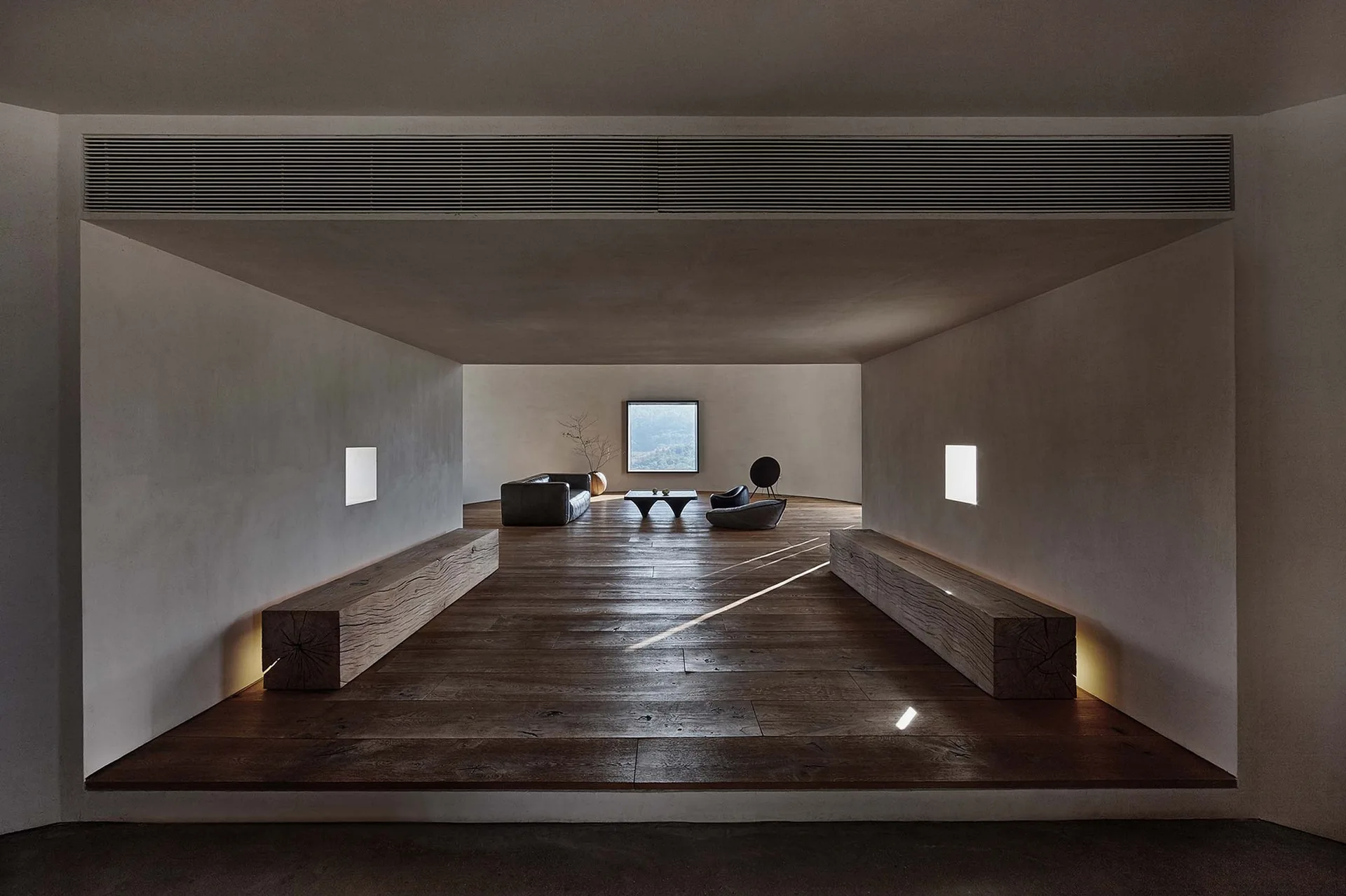 A minimalist corridor featuring dark wood floors and two massive timber block benches leading toward a low-profile living room.