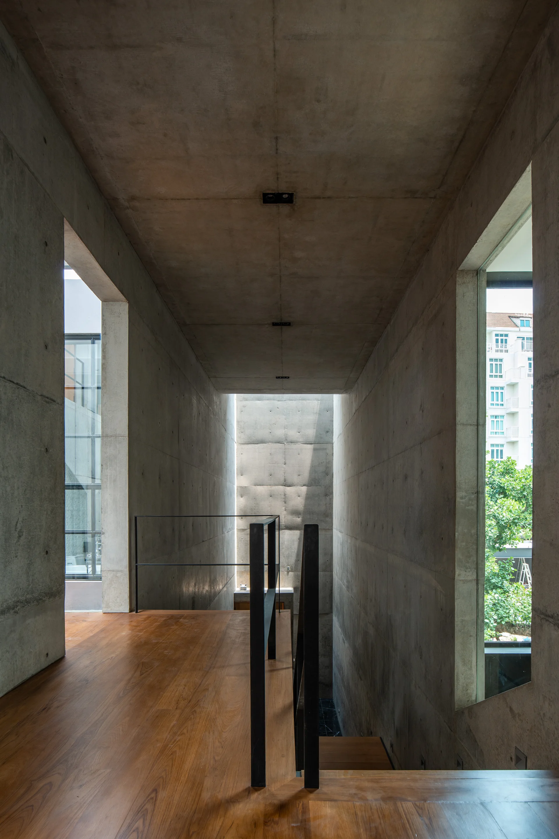 An interior staircase area features tall exposed concrete walls, warm wood flooring, a slim black metal railing, and side windows letting in light.