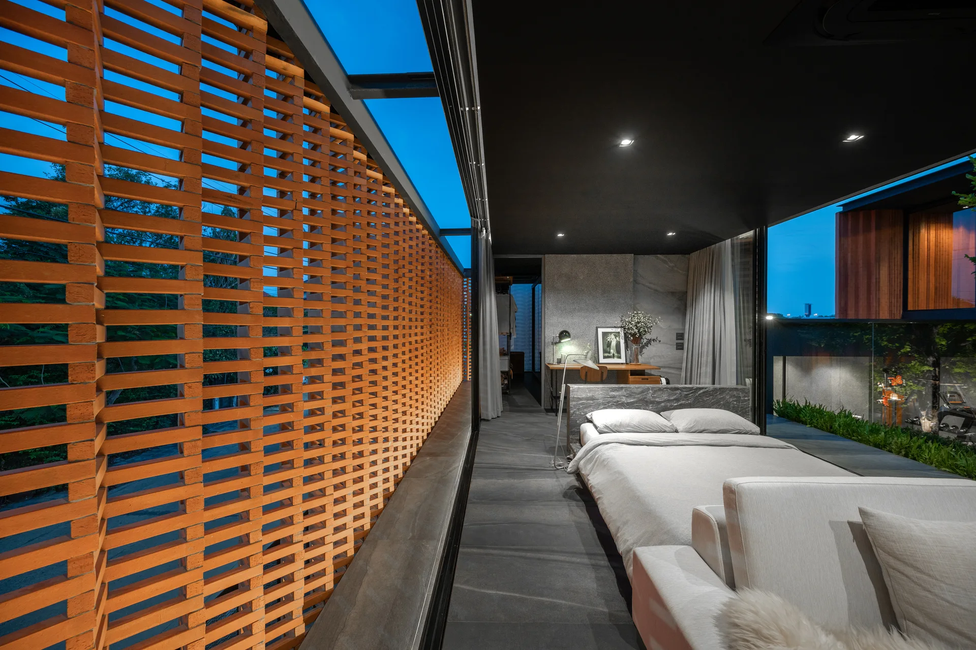 A modern bedroom featuring a low-profile bed, dark stone floors, a black ceiling, and a large perforated terracotta brick screen wall.