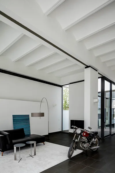 A minimalist living room featuring a black sofa, a blue abstract painting, a light grey rug, and a vintage motorcycle parked on dark tile flooring.