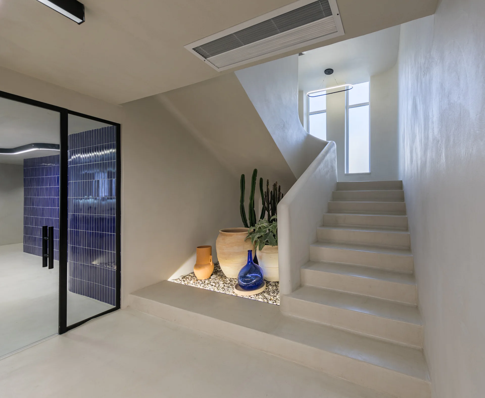 A seamless beige concrete staircase featuring a built-in under-stair planter with gravel, terracotta pots, cacti, and a blue glass vase.