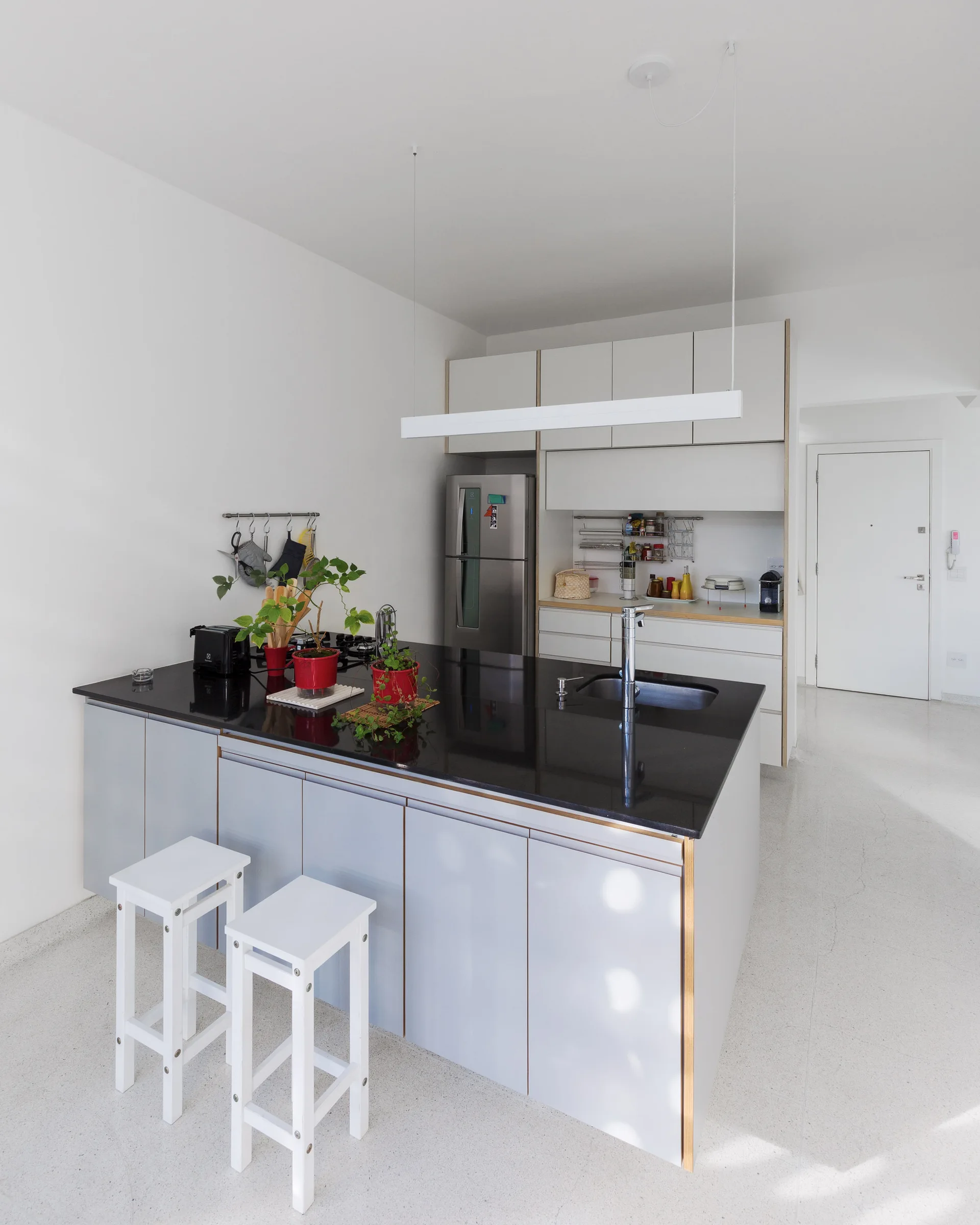 A minimalist kitchen featuring a grey island with a black countertop, two white stools, and a sleek linear pendant light.