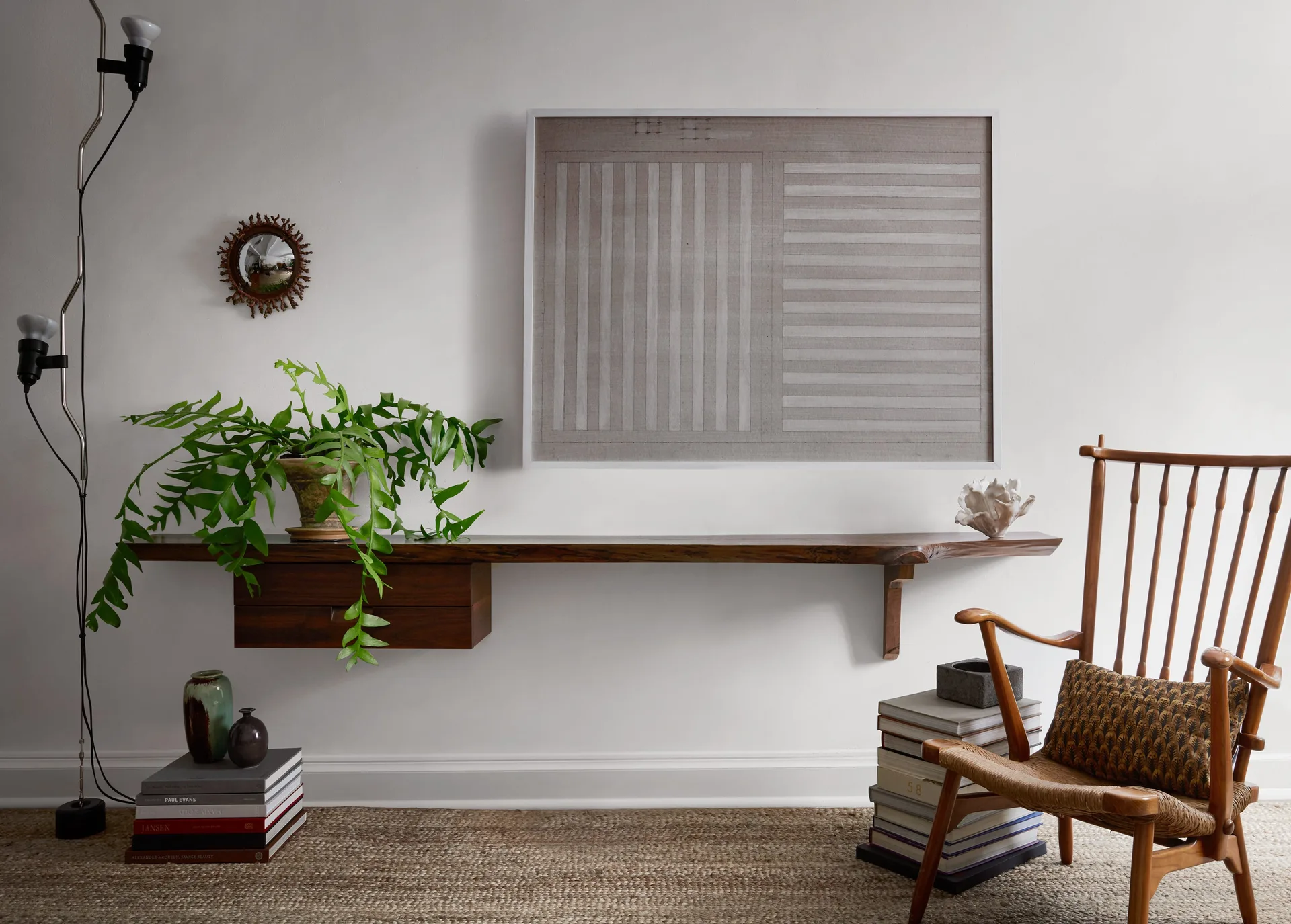 A floating live-edge wood shelf with a drawer hangs next to a wooden spindle chair and stacks of books on a woven rug.