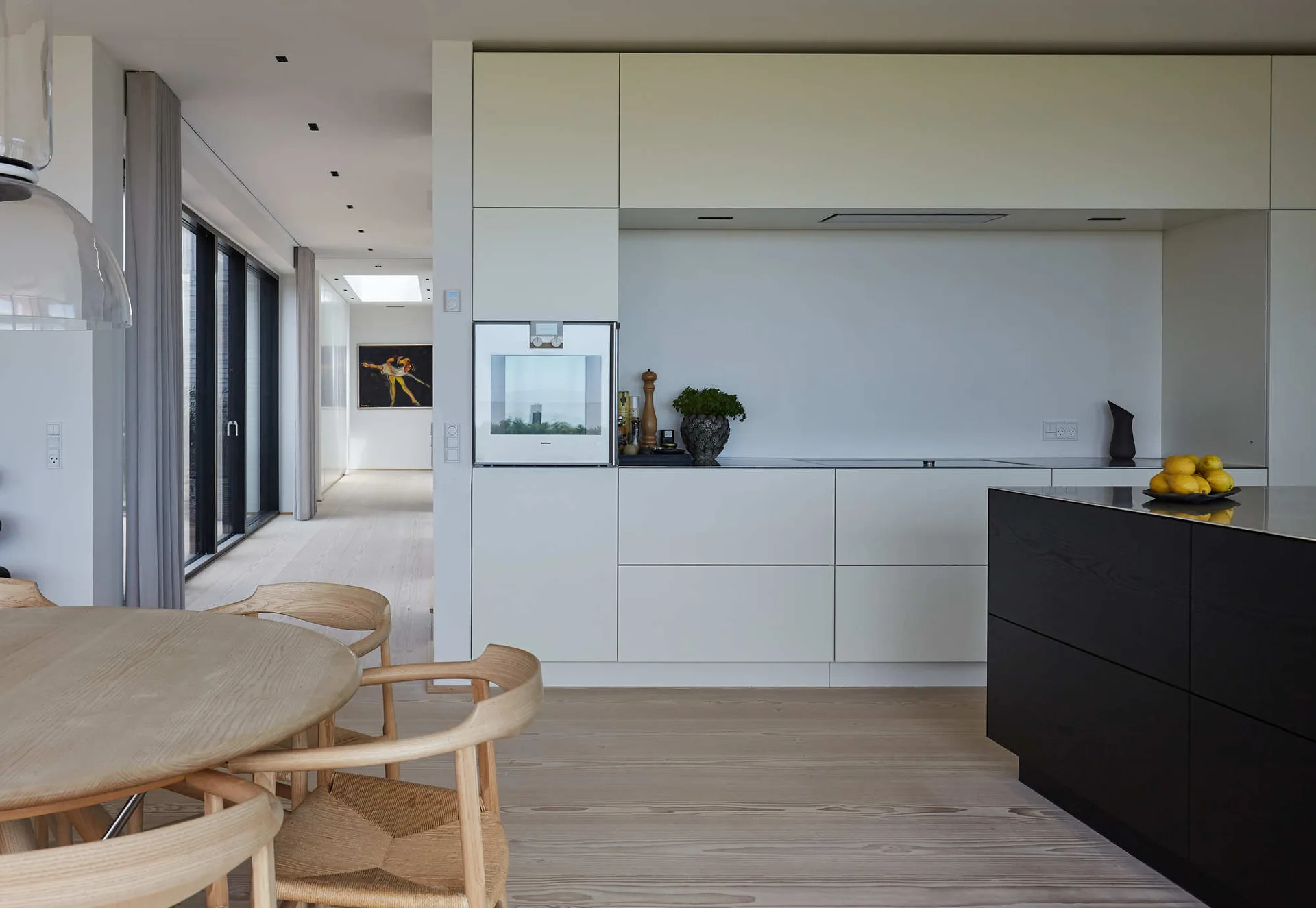 A modern kitchen features flat-panel white cabinets, a contrasting matte black island, light wood floors, and a round wooden dining table.