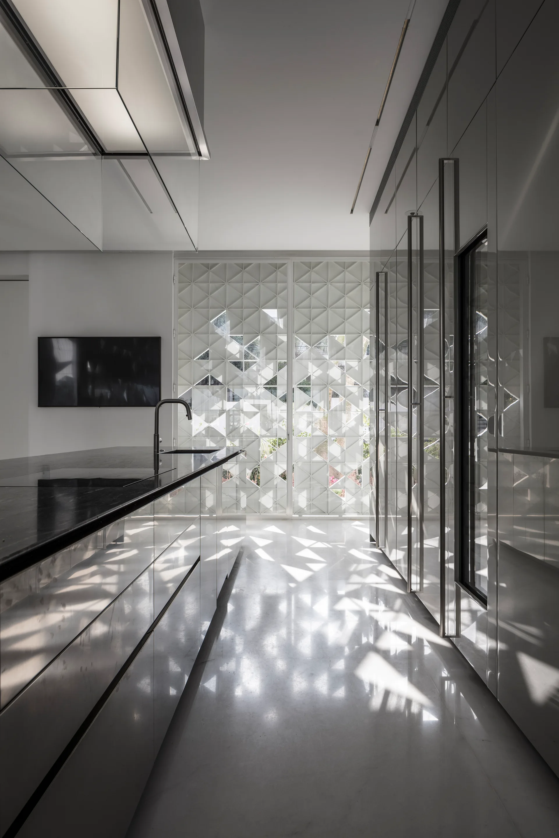 A modern kitchen with high-gloss cabinetry, a dark island, and a white geometric lattice screen filtering natural light onto a polished floor.