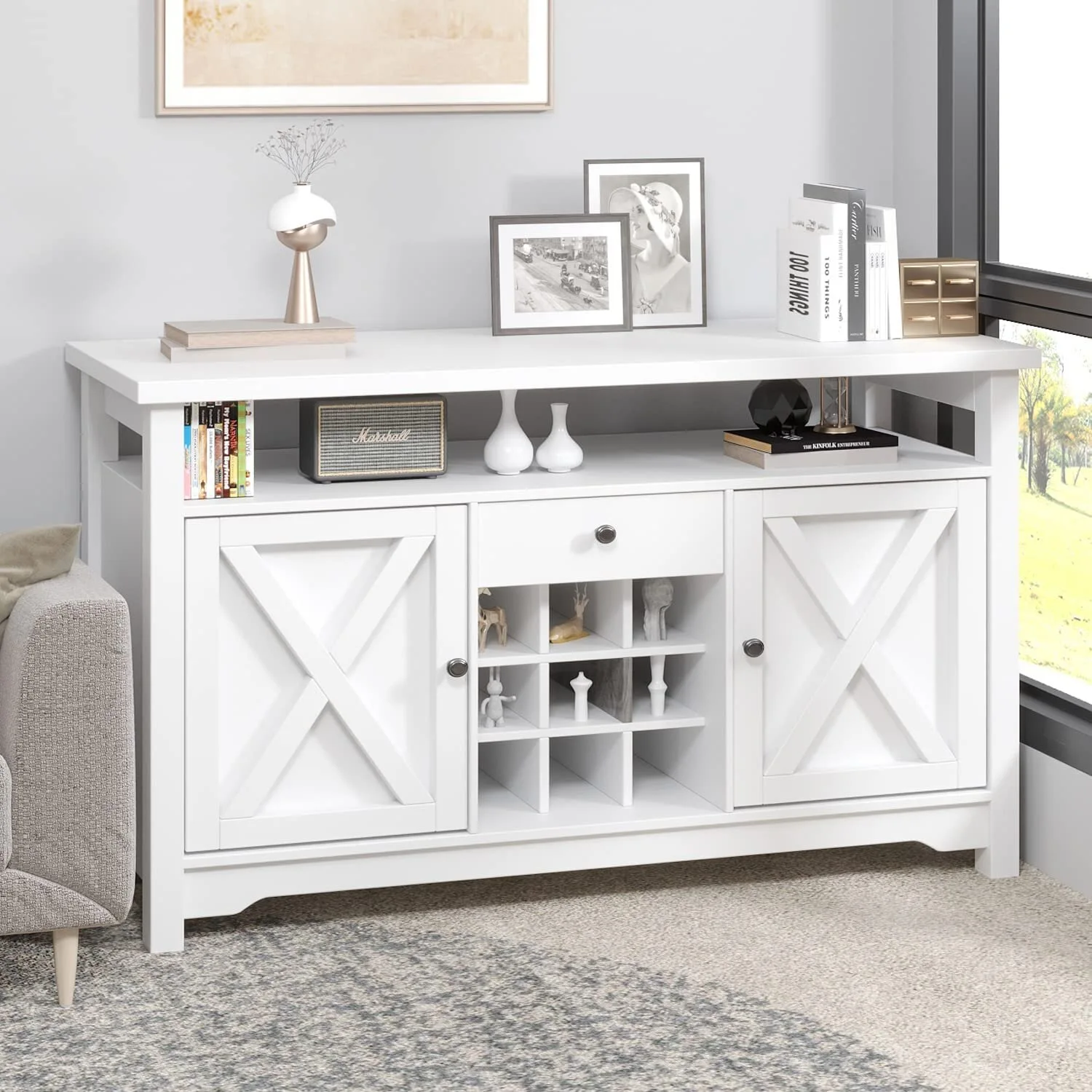 A white wooden console table with farmhouse X-pattern cabinet doors is decorated with books, picture frames, and small vases.