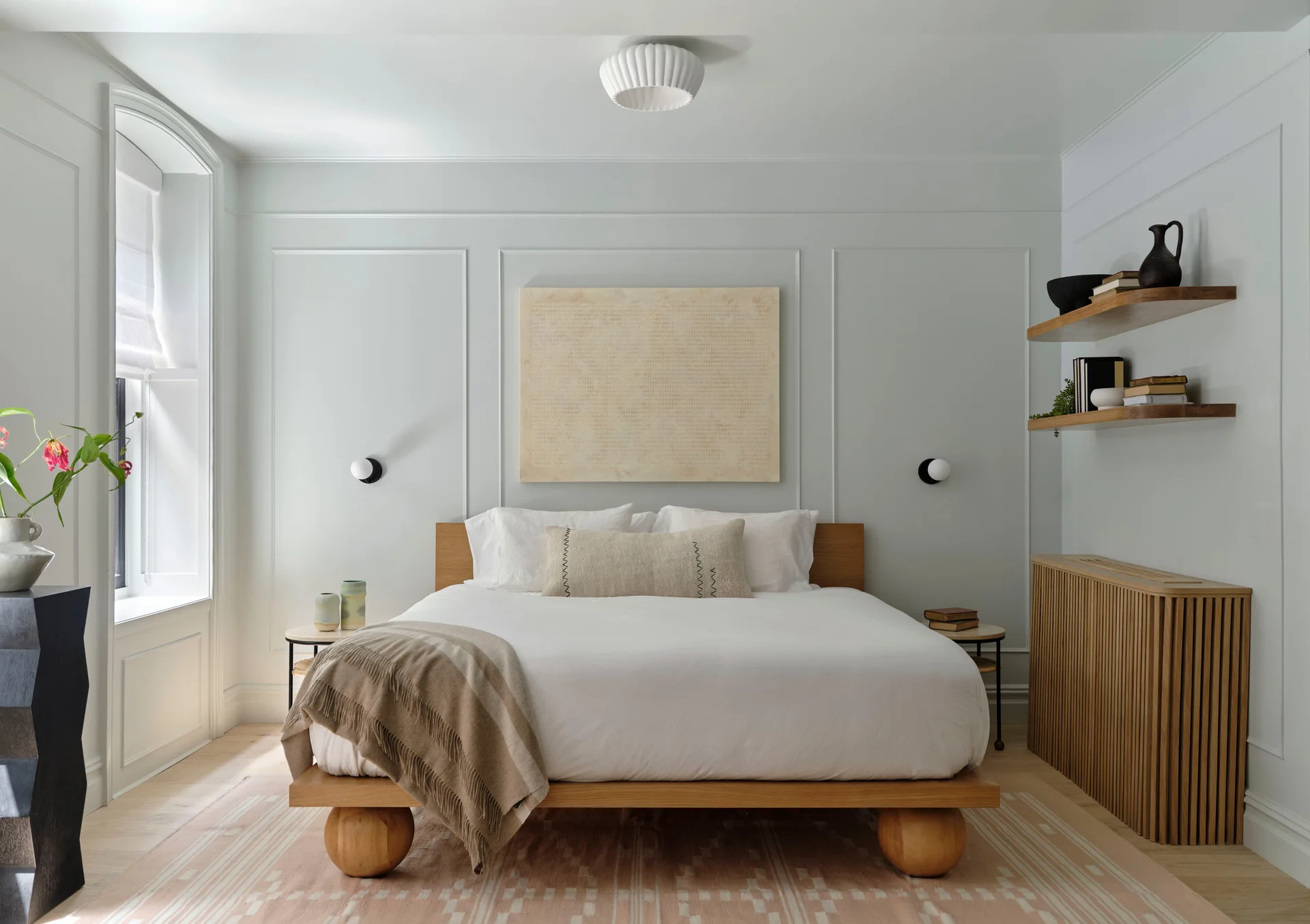 A minimalist bedroom featuring a low-profile wooden platform bed, light blue paneled walls, and floating wood shelves.