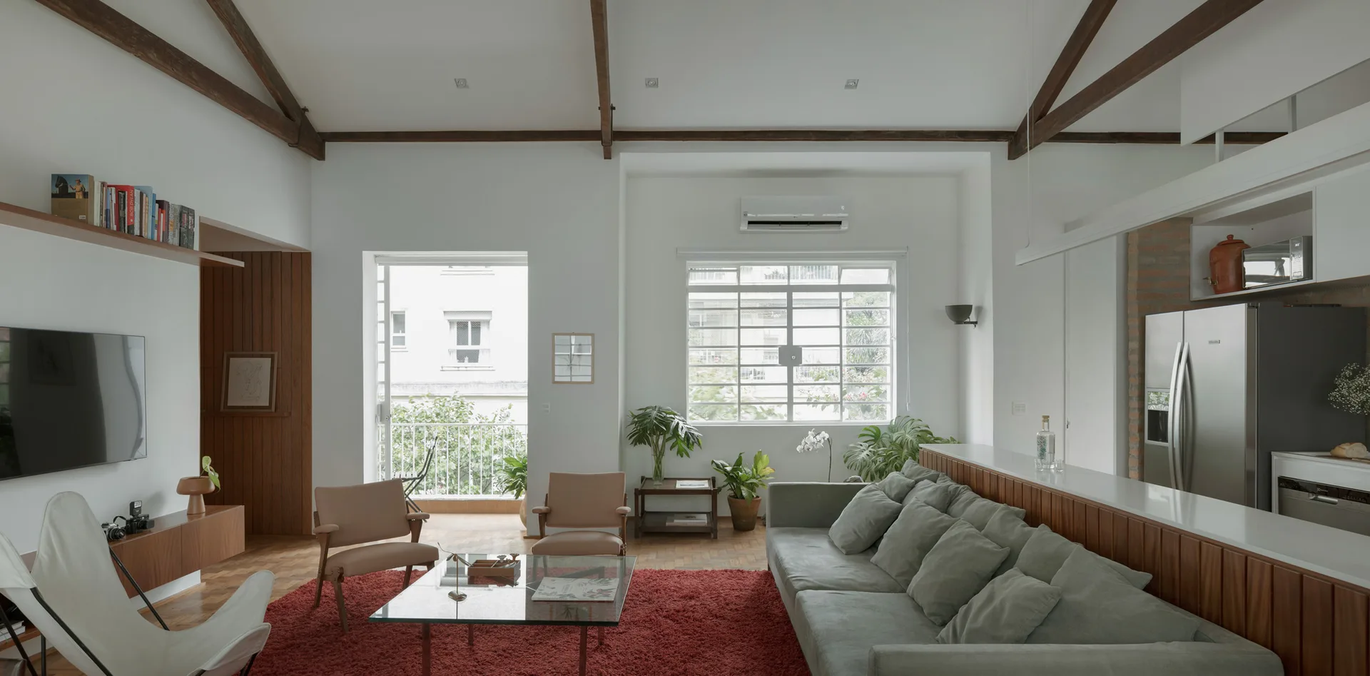 A bright living room features a grey sofa, red shag rug, and mid-century modern armchairs under a vaulted ceiling with exposed wood beams.