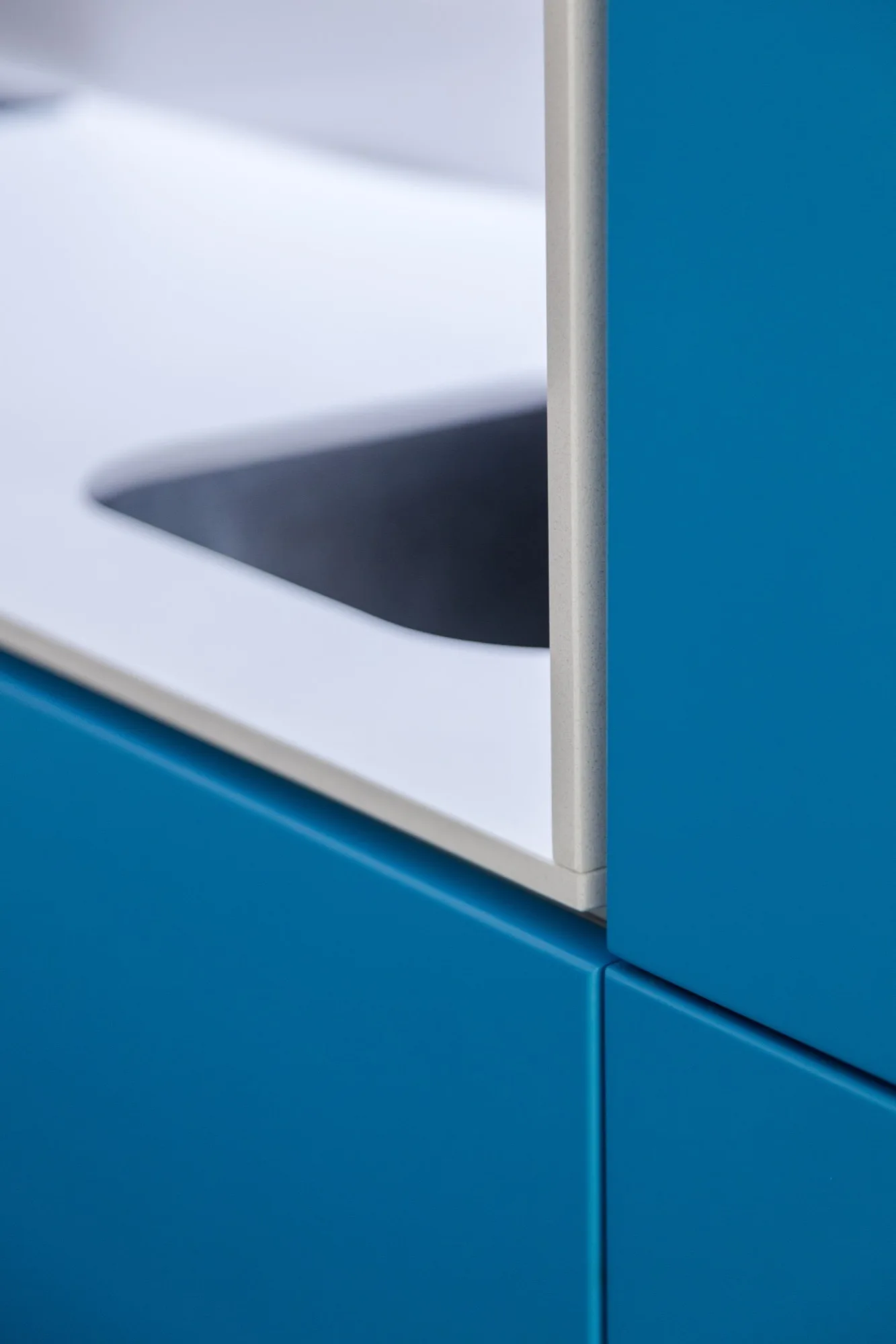 A detailed close-up of vibrant matte blue cabinet fronts meeting a slim white countertop edge.