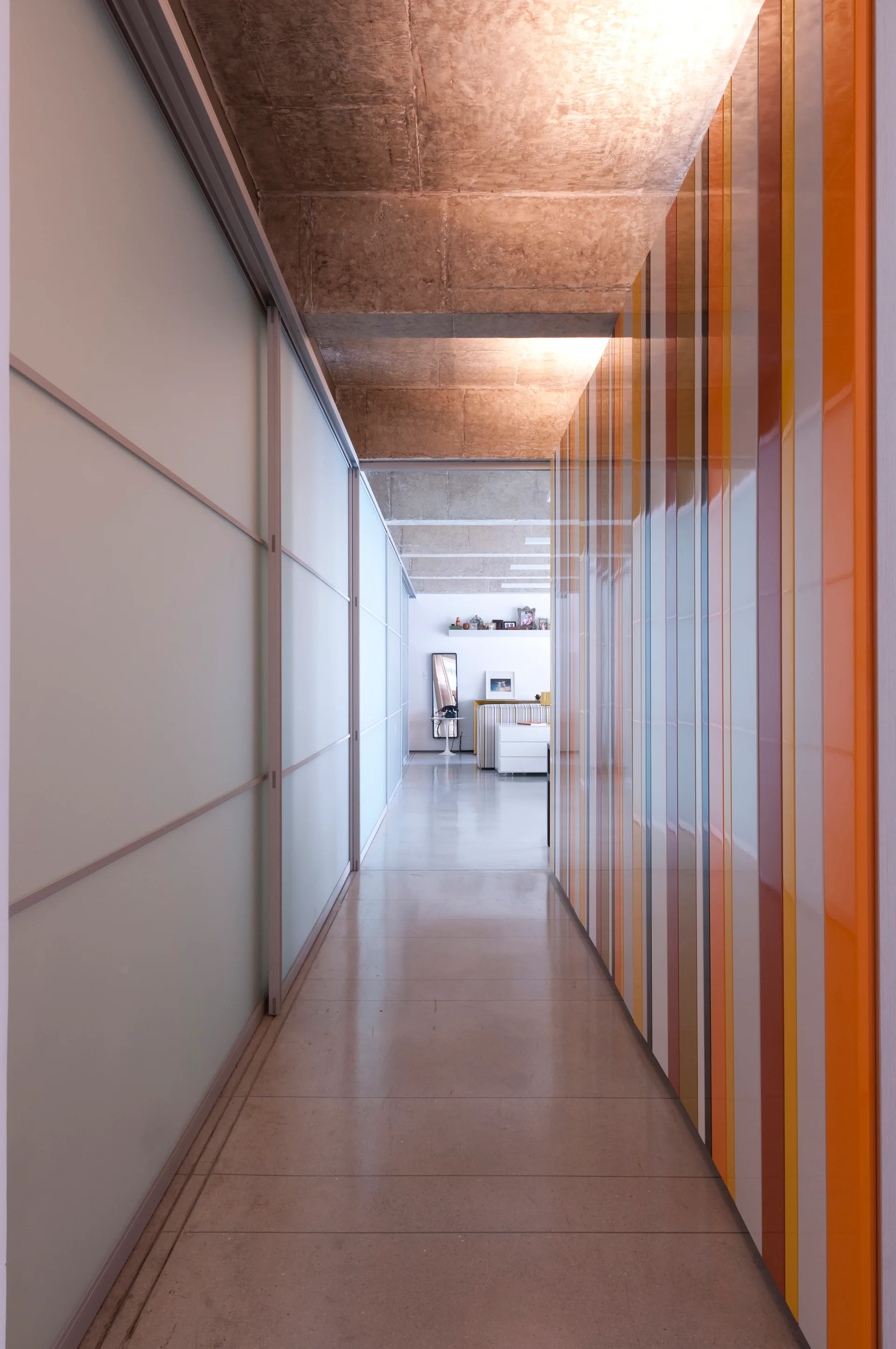A long hallway features a colorful vertical striped wall panel, frosted glass sliding doors, polished concrete flooring, and an exposed raw concrete ceiling.