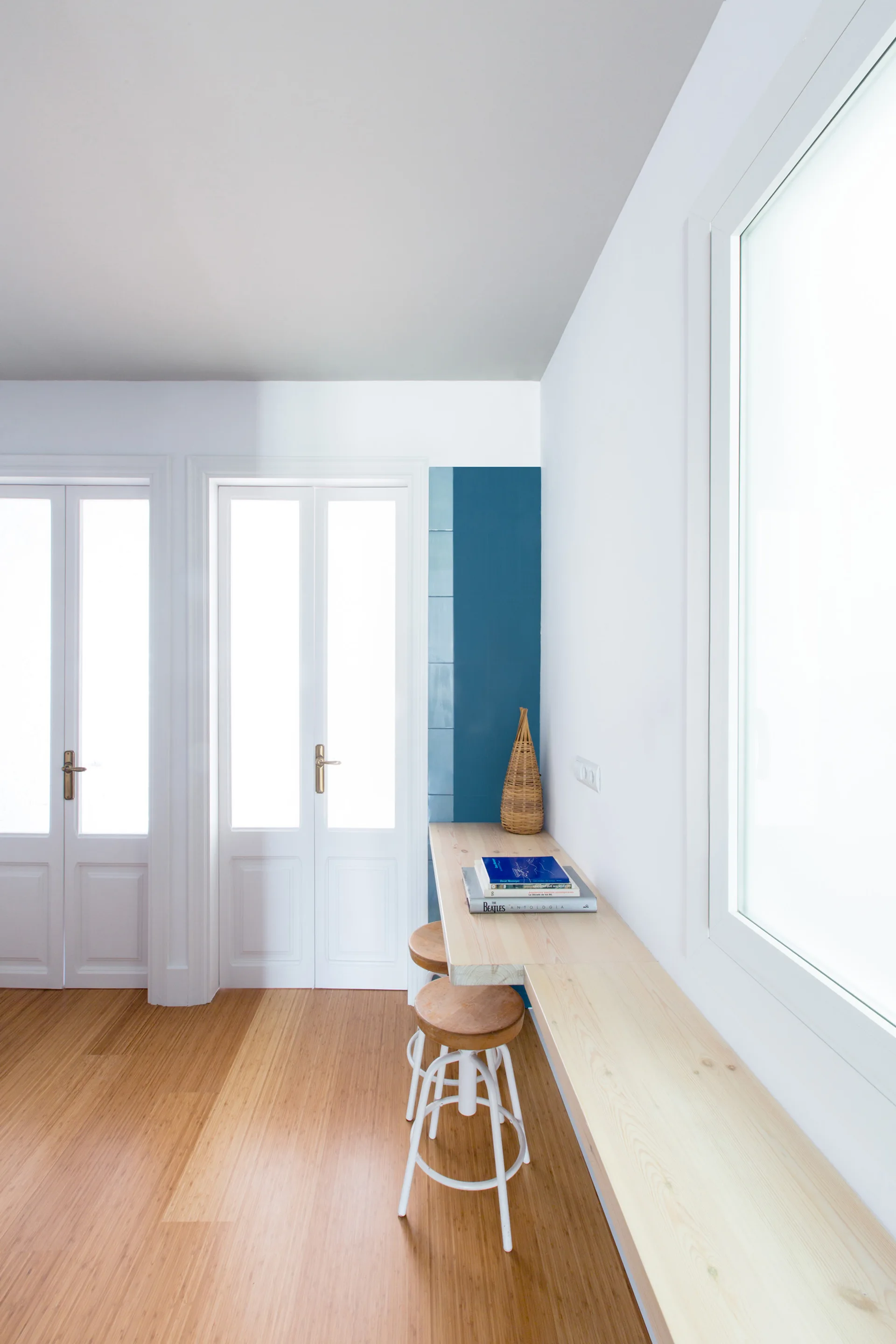A bright hallway features a long floating wood console table, two white doors with glass panes, and a vertical strip of blue wall tiles.