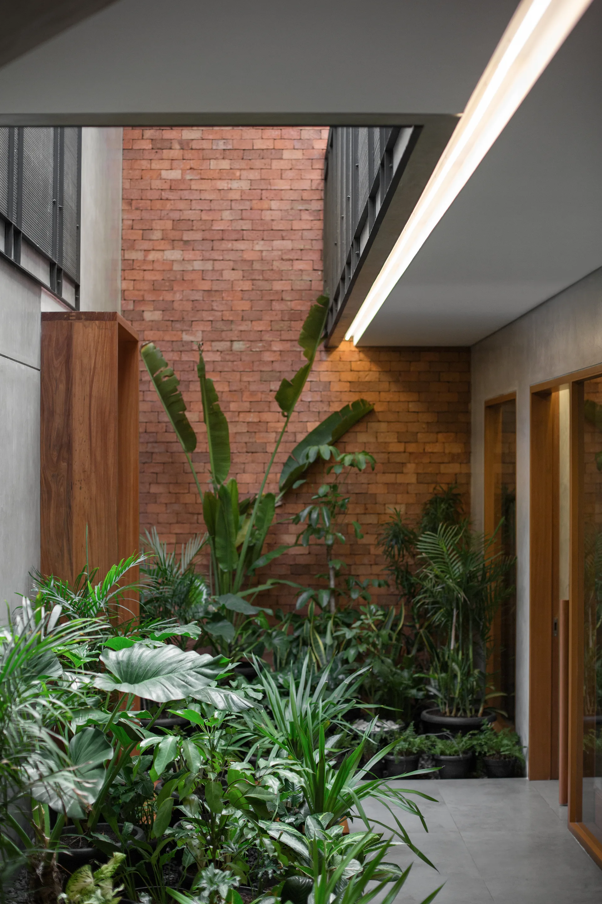 A modern indoor-outdoor courtyard featuring a tall red brick wall, smooth concrete flooring, and an abundance of leafy green potted plants.