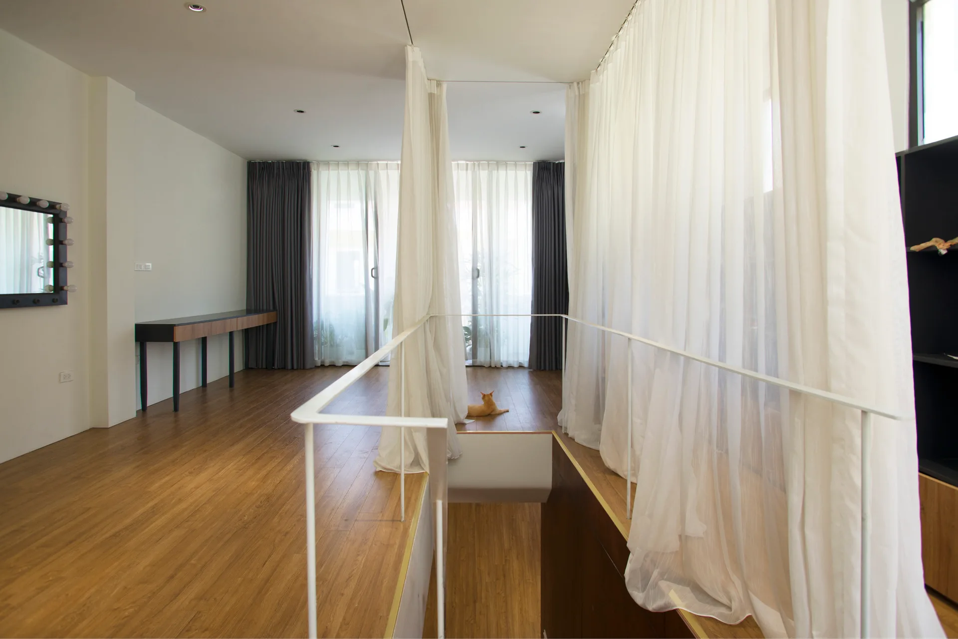 A bright modern staircase landing featuring wood floors, a white metal safety railing, and floor-to-ceiling sheer white curtains.