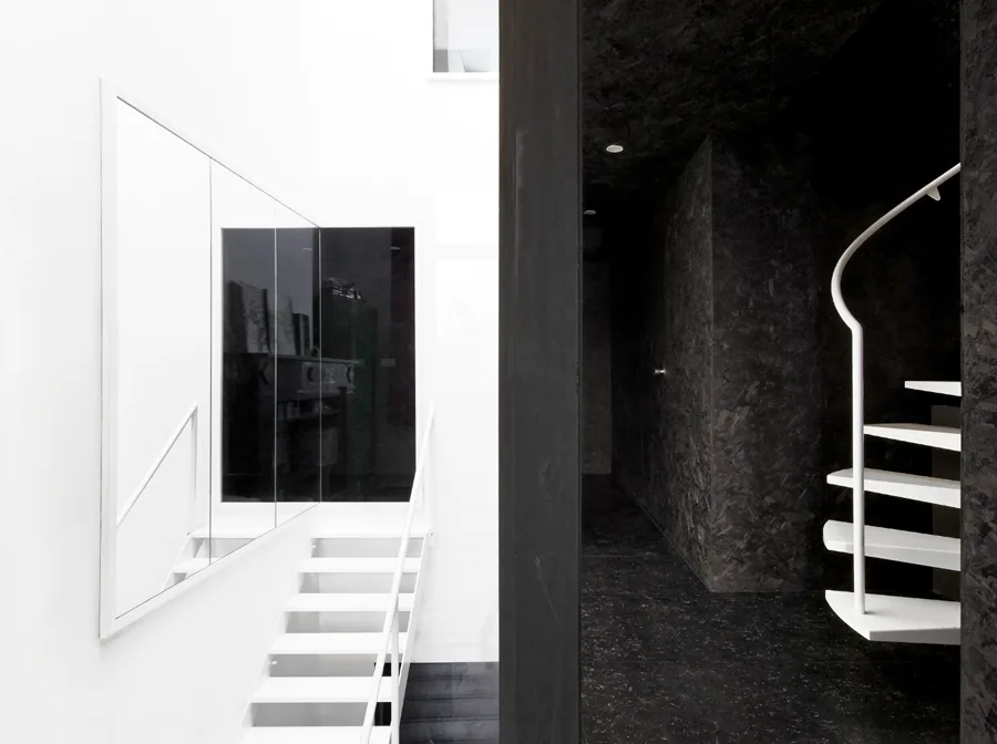 A stark interior split shows a bright white stairwell with metal stairs and a mirror next to a dark, textured black hallway.