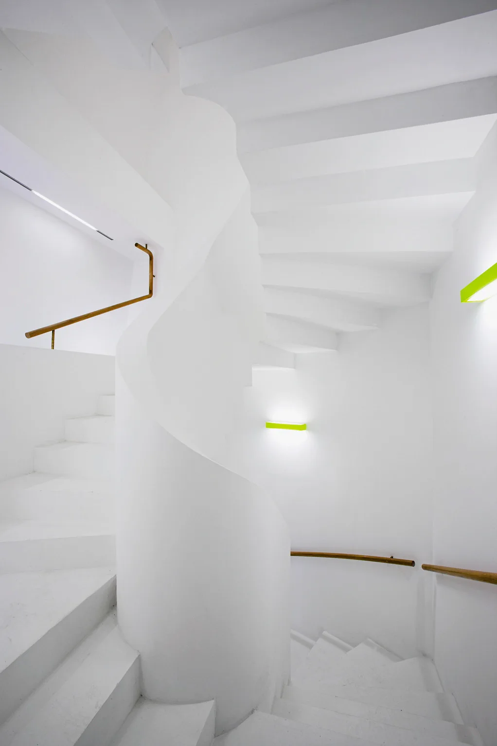 A winding white spiral staircase featuring a curved smooth plaster railing, a thin wooden handrail, and horizontal lime green wall-mounted lights.