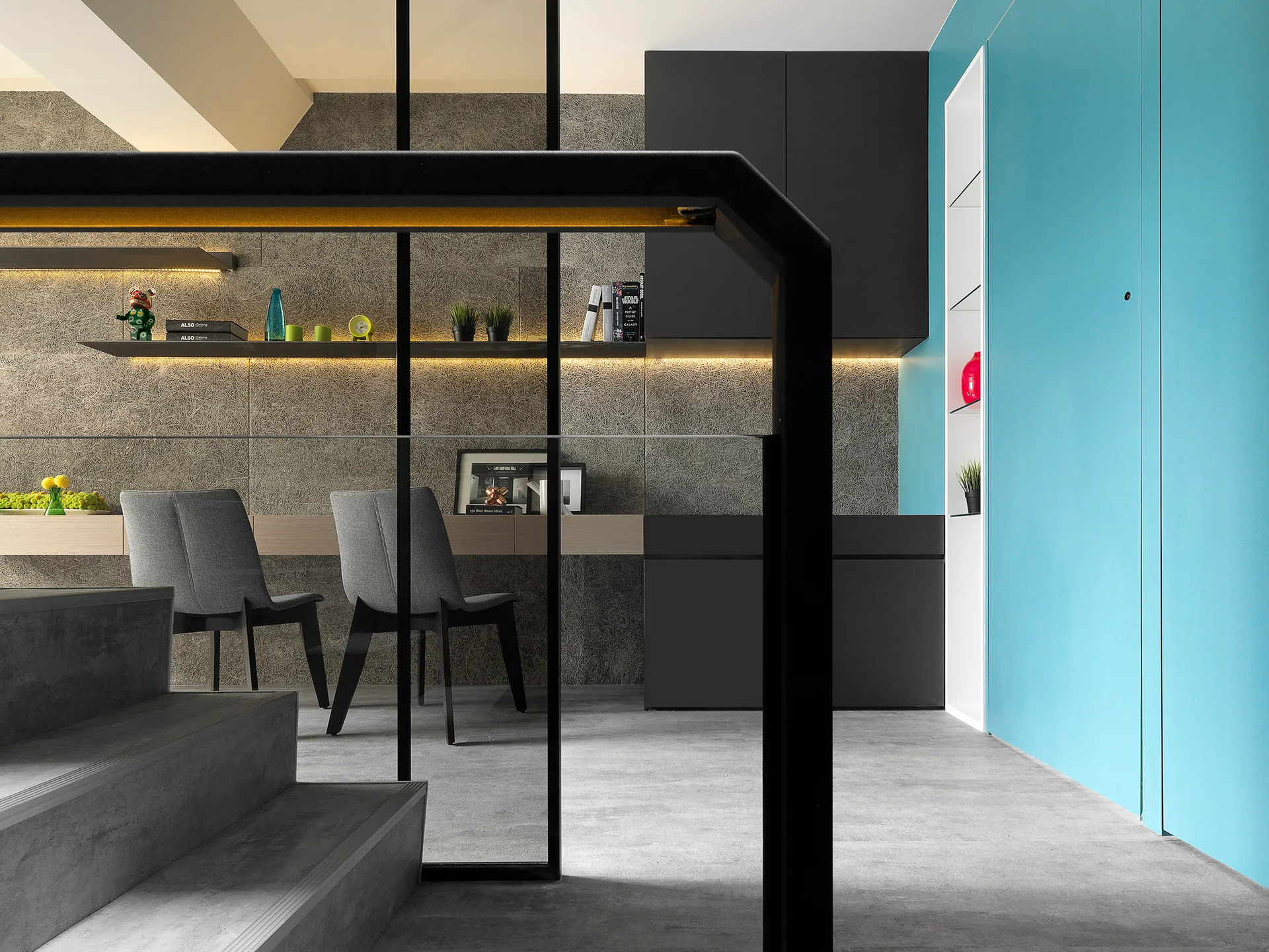 Concrete steps and a black railing frame a modern workspace with a floating wooden desk, gray chairs, and a bright turquoise accent wall.