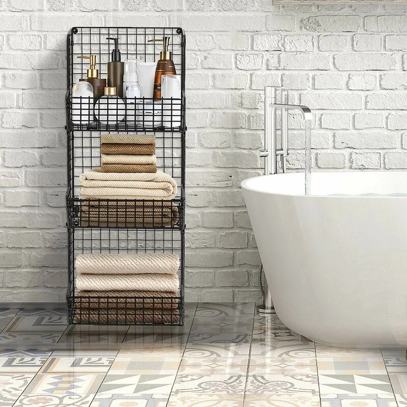 A three-tier black metal wire storage rack holding towels and toiletries stands next to a white soaking tub against a painted brick wall.