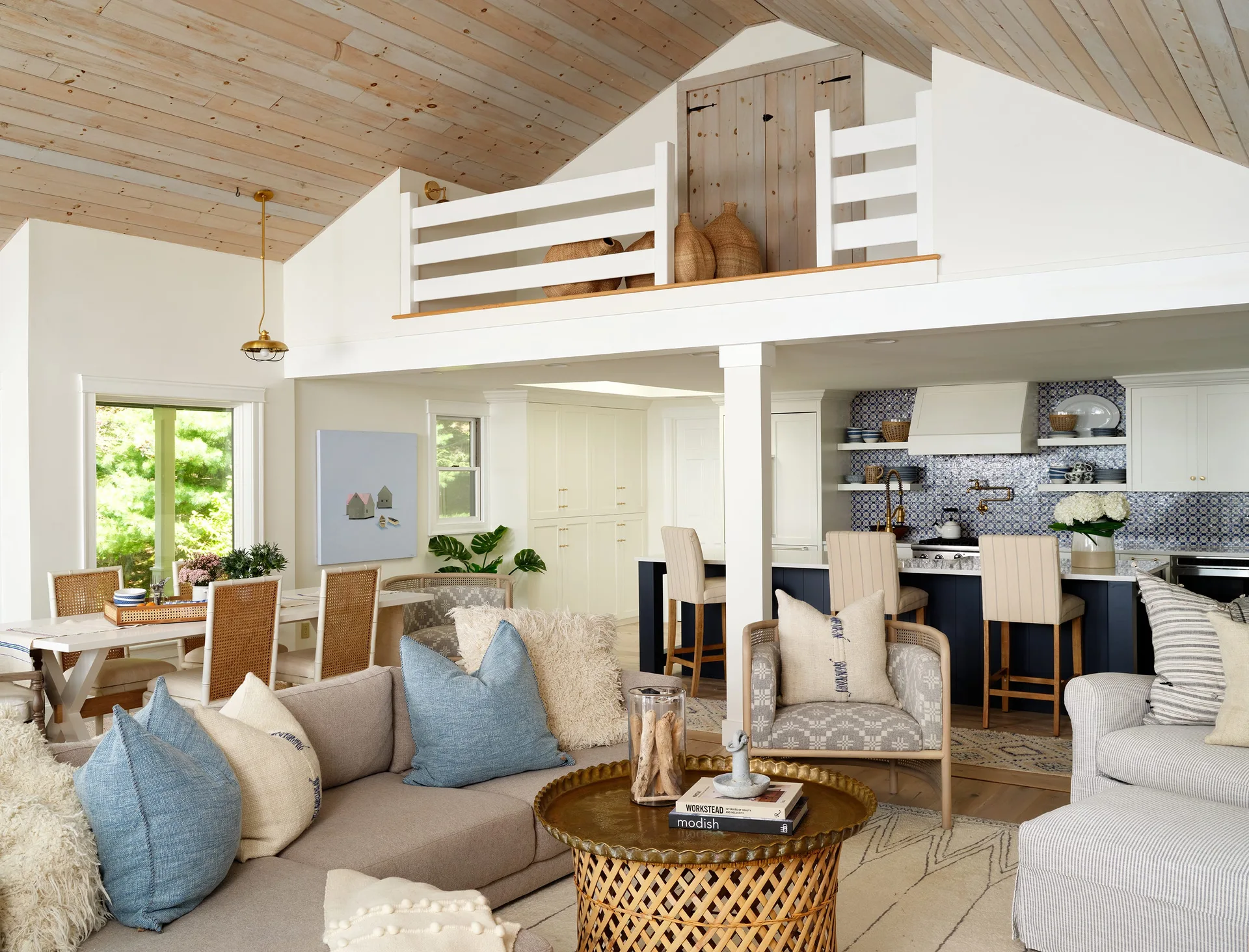 An open living room and kitchen features a vaulted ceiling, a loft mezzanine, and a blue tile backsplash.