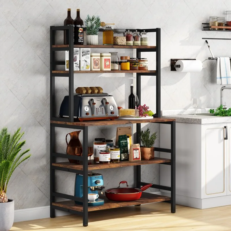 An industrial black metal and wood bakers rack stands next to a white kitchen counter, holding a toaster, coffee maker, and jars.